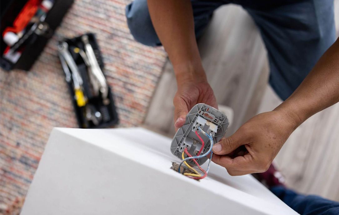 Persona che collega un dispositivo su una superficie bianca, con gli attrezzi in una cassetta degli attrezzi aperta nelle vicinanze.