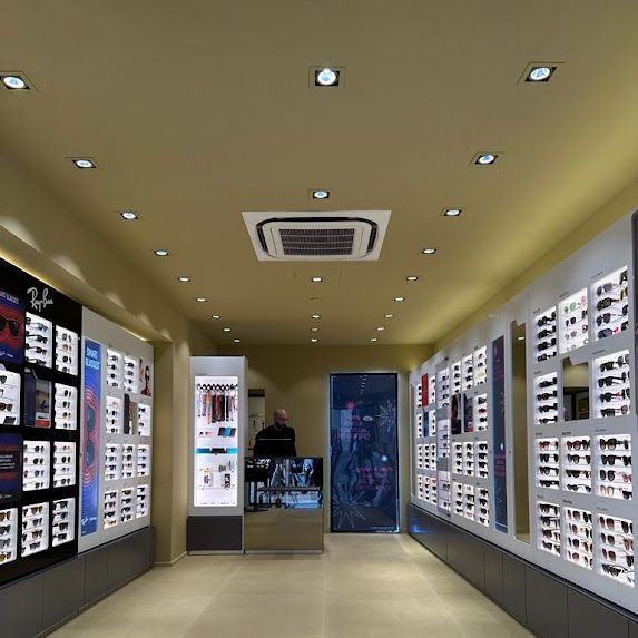Interno di un negozio di occhiali con più espositori di occhiali e una persona in piedi vicino a uno specchio.