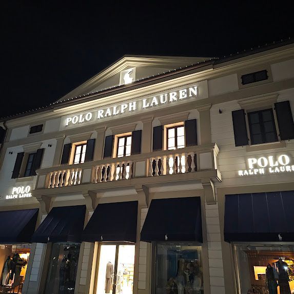 Facciata del negozio Polo Ralph Lauren di notte, con insegna illuminata e tende da sole, edificio in pietra chiara.