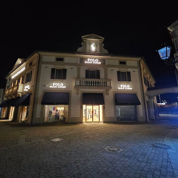 Esterno notturno di un negozio Polo Ralph Lauren con insegne illuminate e tende da sole.