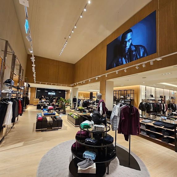 Interno di un negozio Hugo Boss. Abbigliamento maschile esposto su scaffali e scaffali. Grande display digitale.
