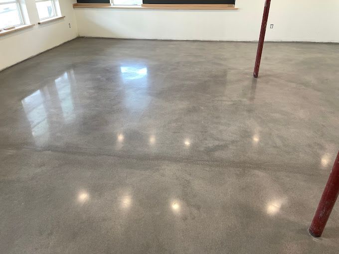Polished concrete floor in a bright, empty room, reflecting light from windows. Two red poles stand.
