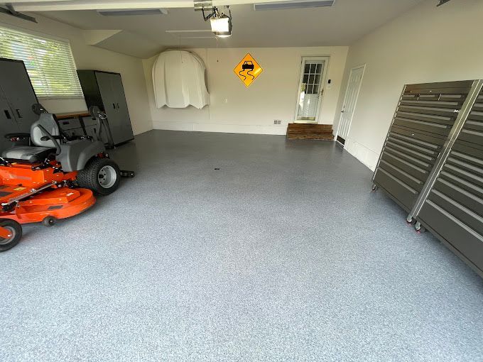 A clean, modern garage with a gray epoxy floor, a riding mower, and tool cabinets.