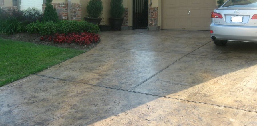 A concrete driveway with a car parked in front of a house with landscaping on the left.