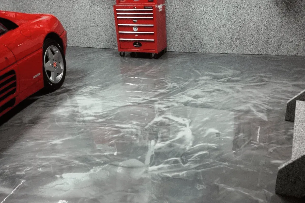 Red sports car and red tool cabinet in a garage with epoxy marbled flooring.