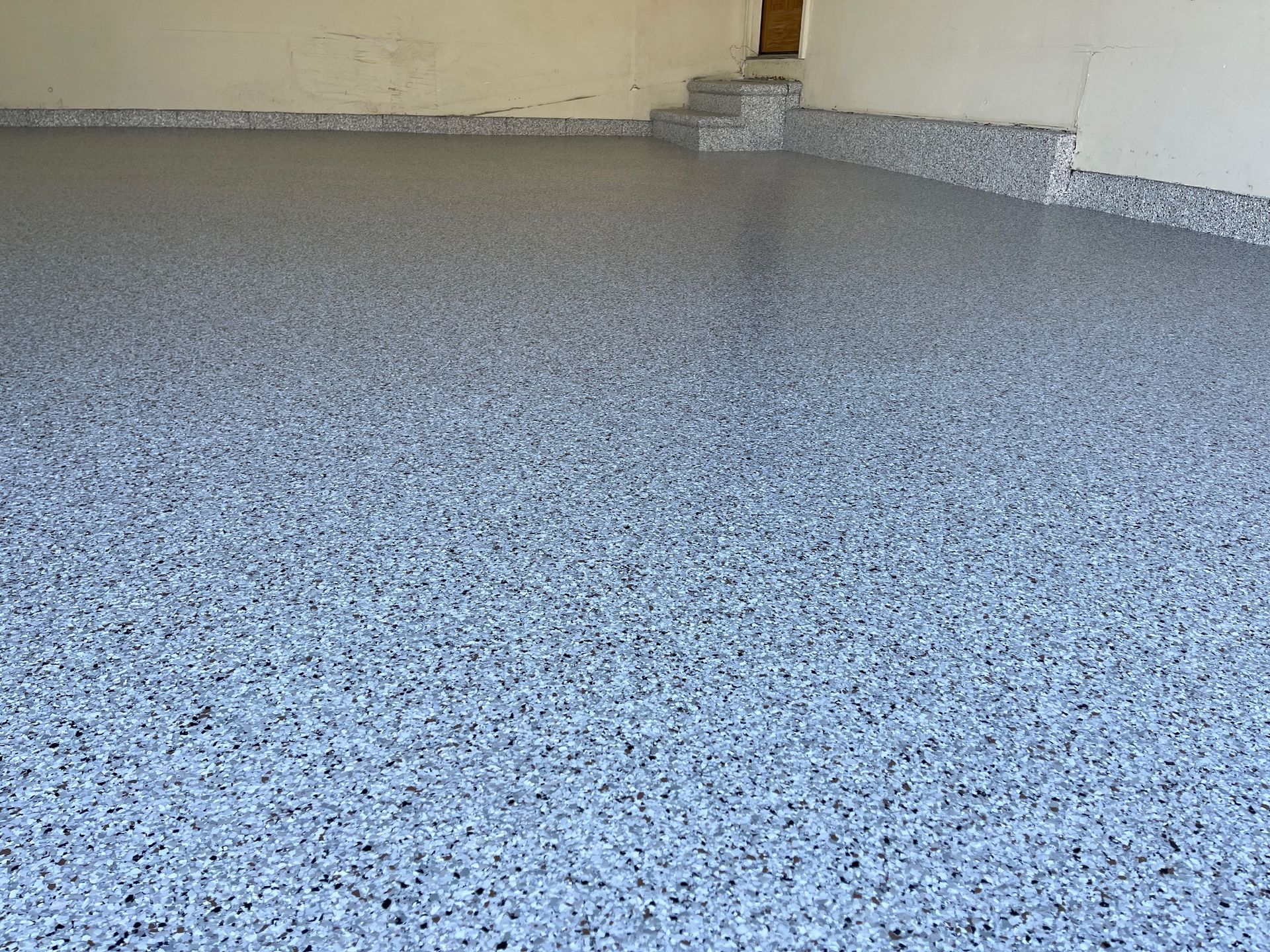 Epoxy-coated garage floor with gray and white chips, reflecting light.