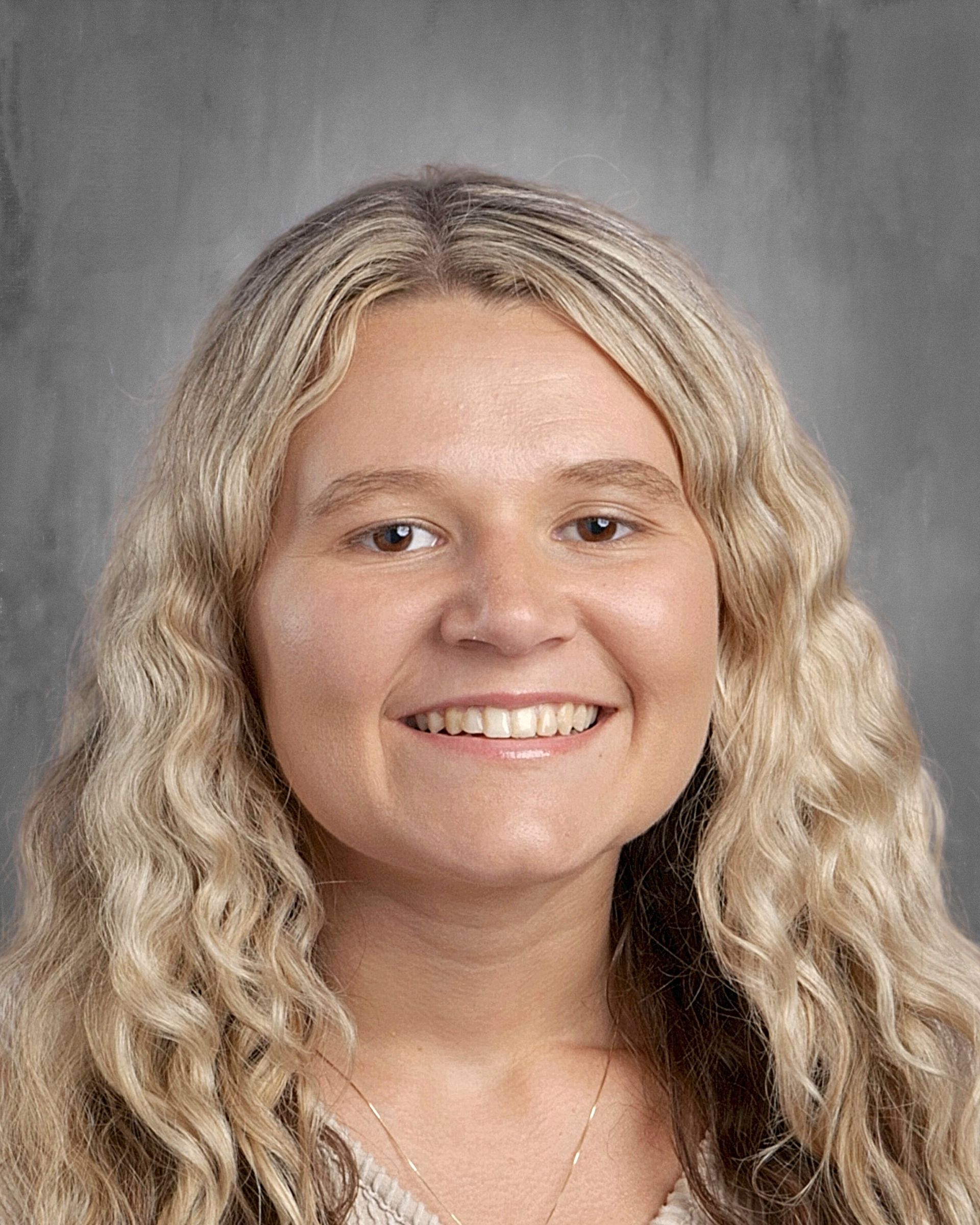 Smiling woman with curly black hair in a floral top, against a gray background.