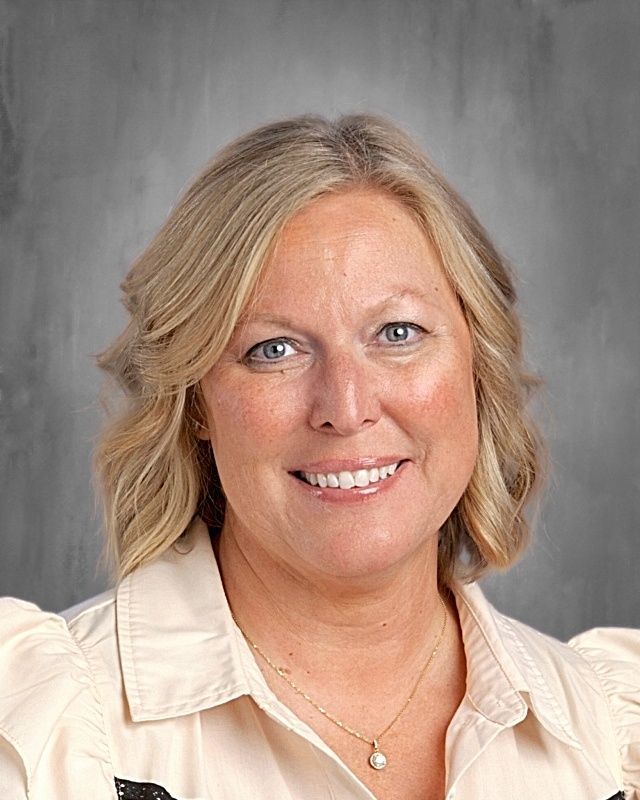 Woman with blonde hair, glasses, and a smile, against a gray backdrop.