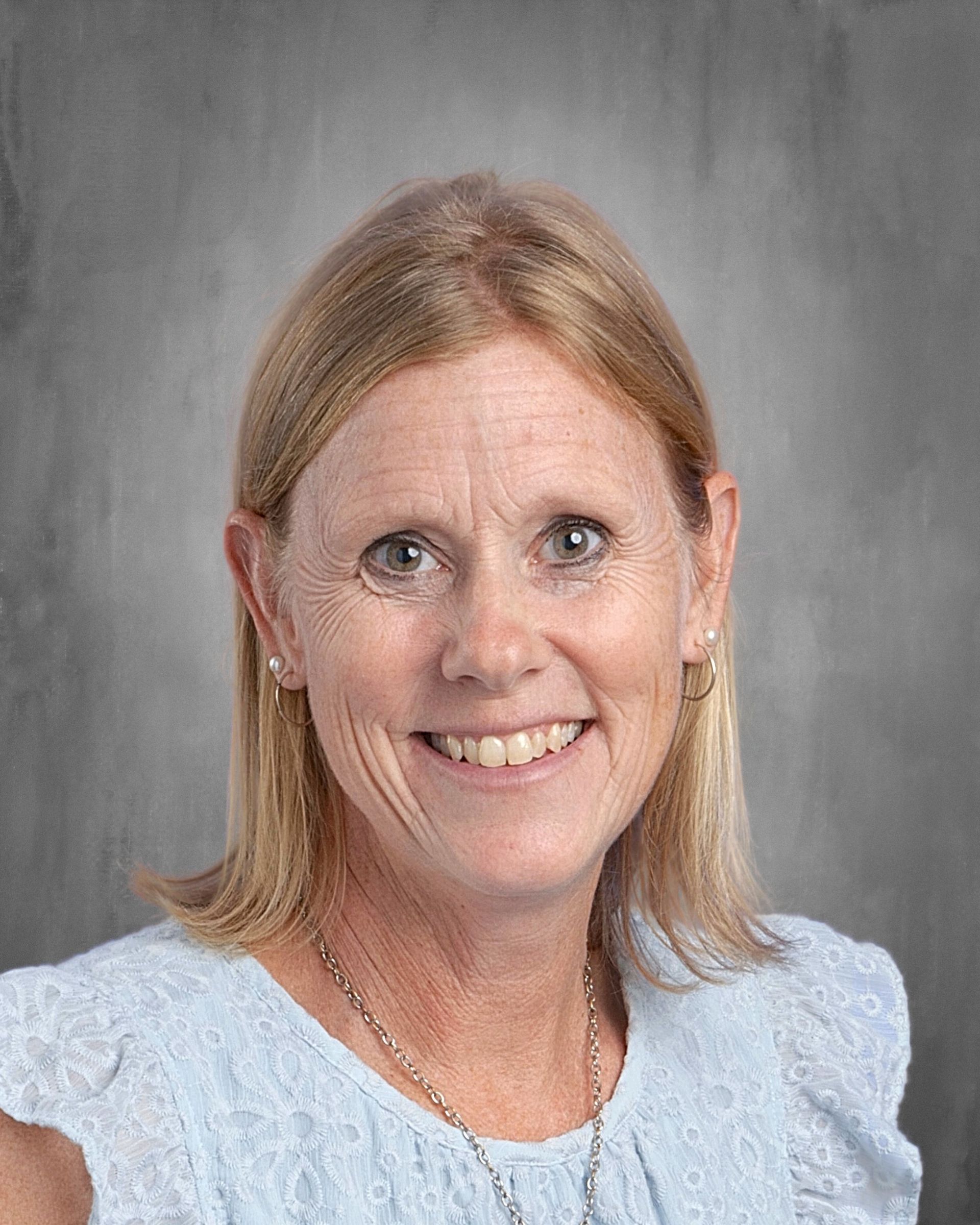 Blond woman smiling at the camera, wearing a pink shirt, against a gray background.