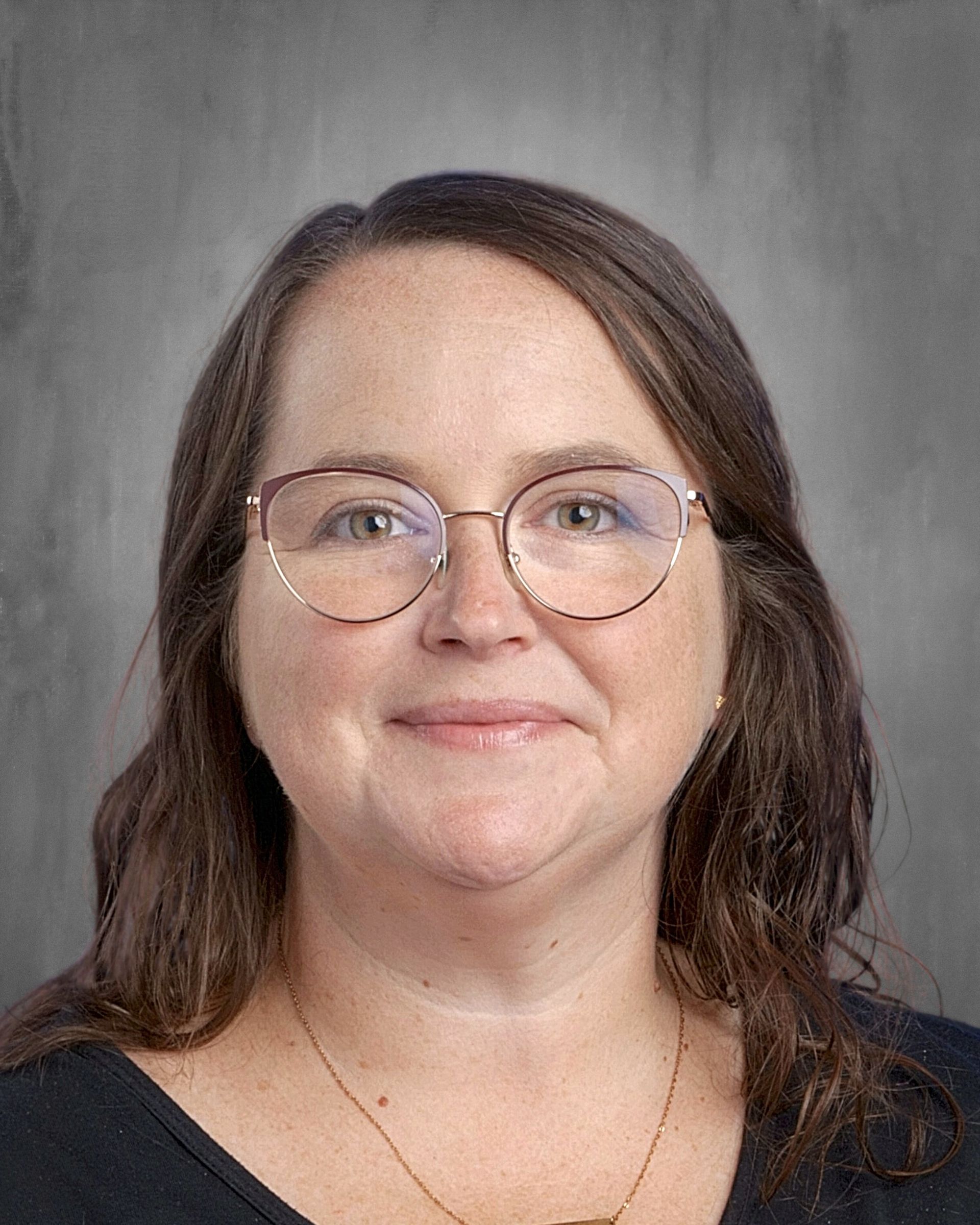 Woman with light skin, brown hair, smiling, wearing a yellow top, against a gray backdrop.