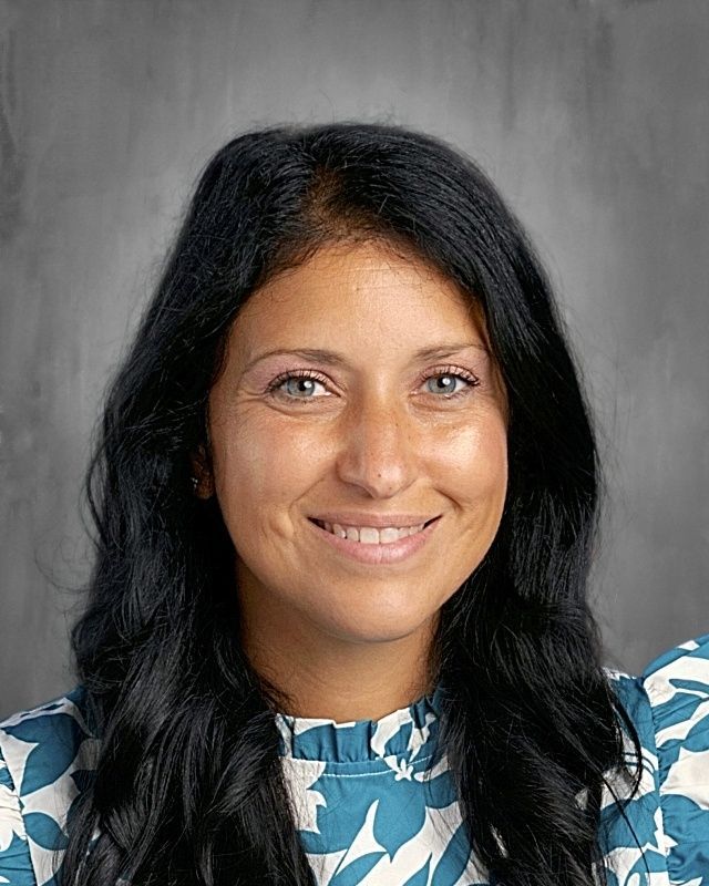 Woman with long brown hair smiles at the camera in front of a gray backdrop.