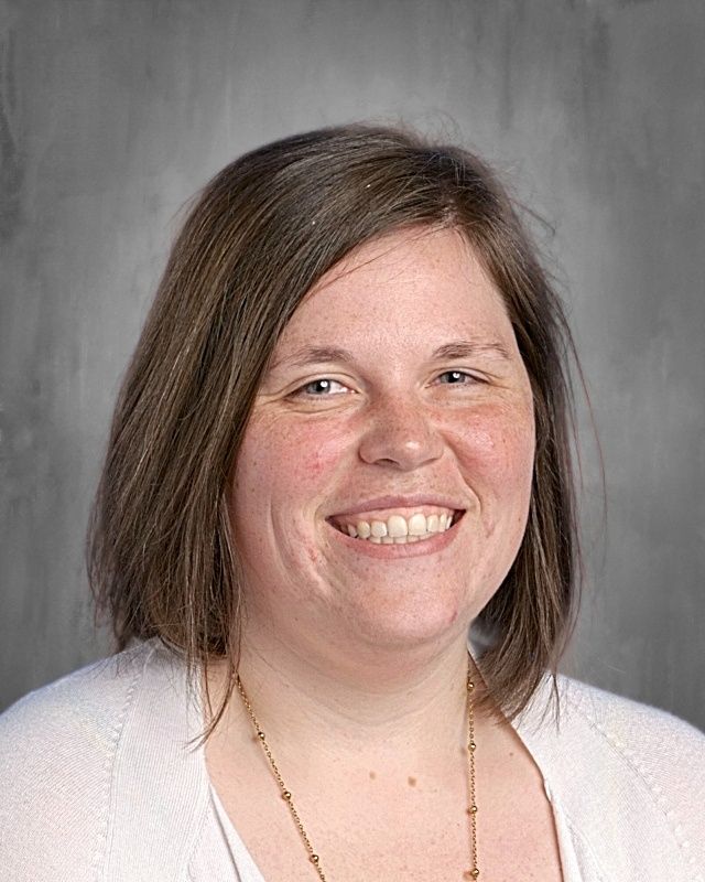 Woman with long brown hair smiling at the camera; wearing a white cardigan.