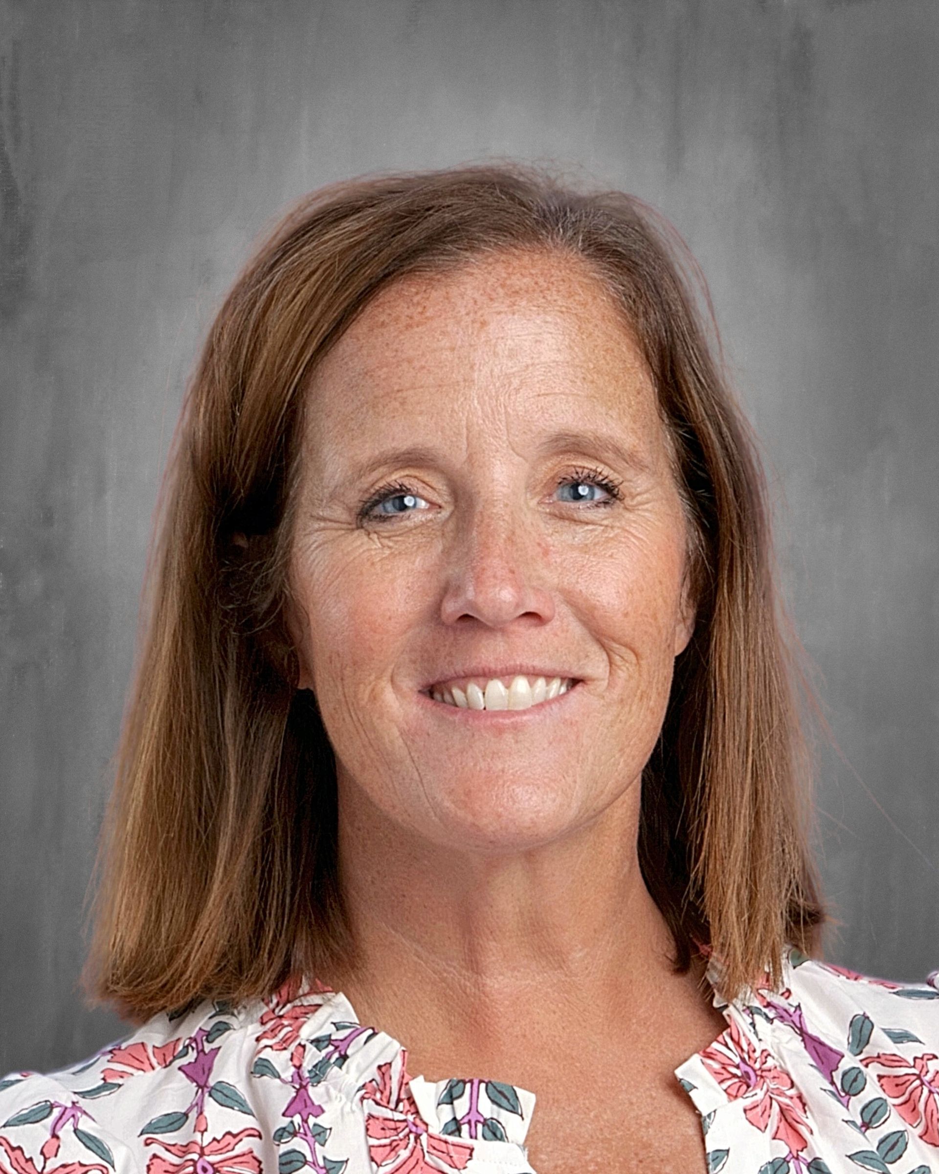 Woman with short blonde hair smiles at the camera, wearing a floral-print blouse.