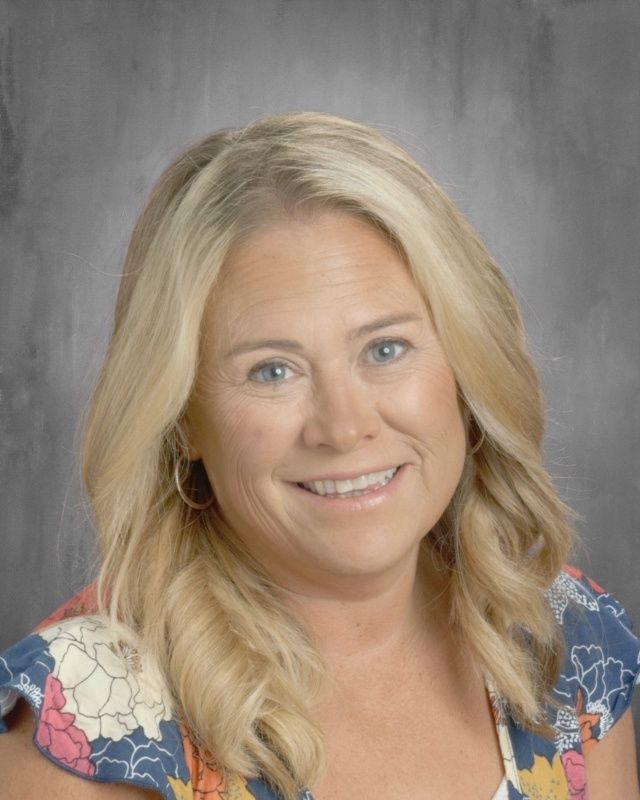Blonde woman smiling, floral top. Dark background.