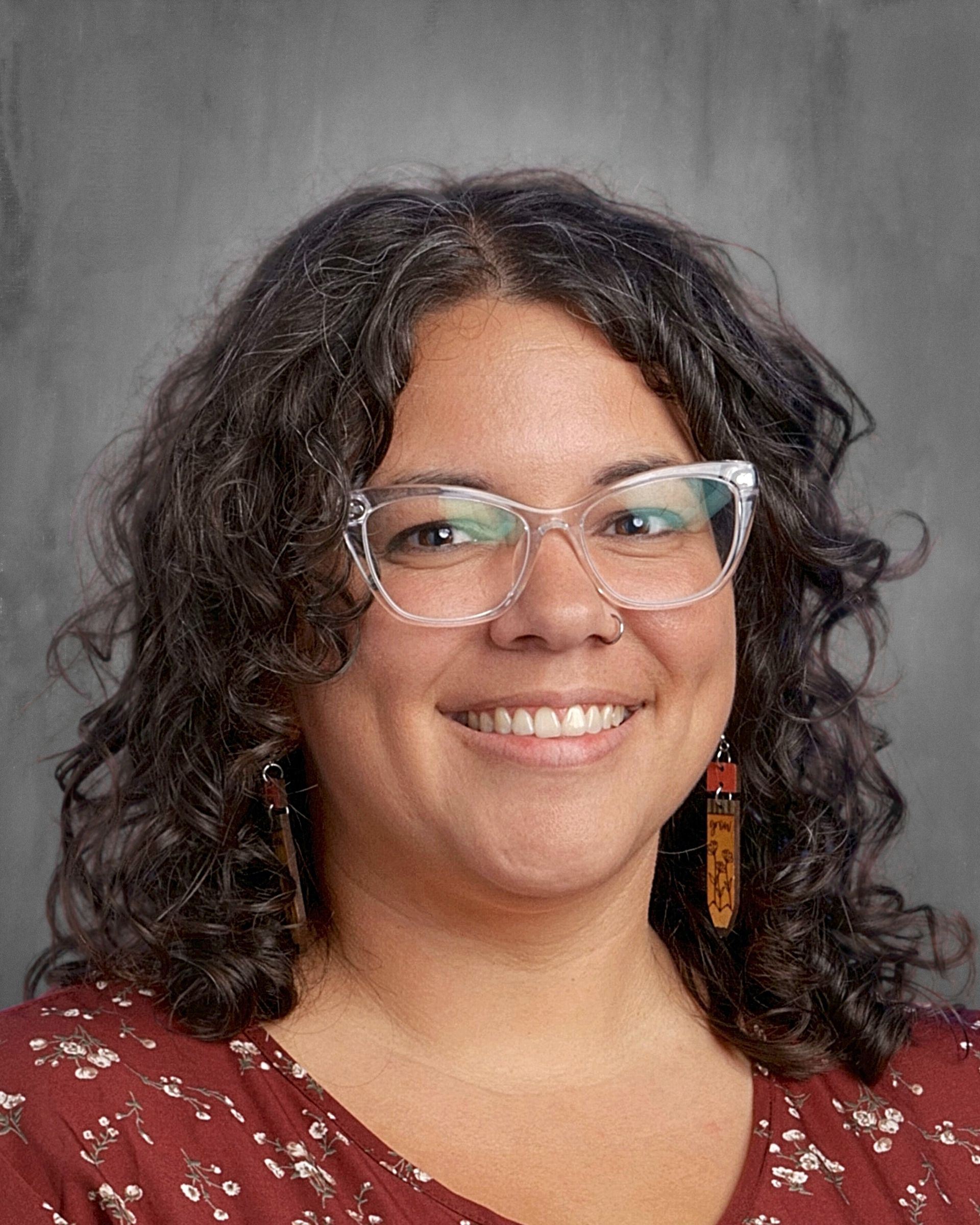 Woman with short blonde hair smiles at the camera, wearing a floral-print blouse.