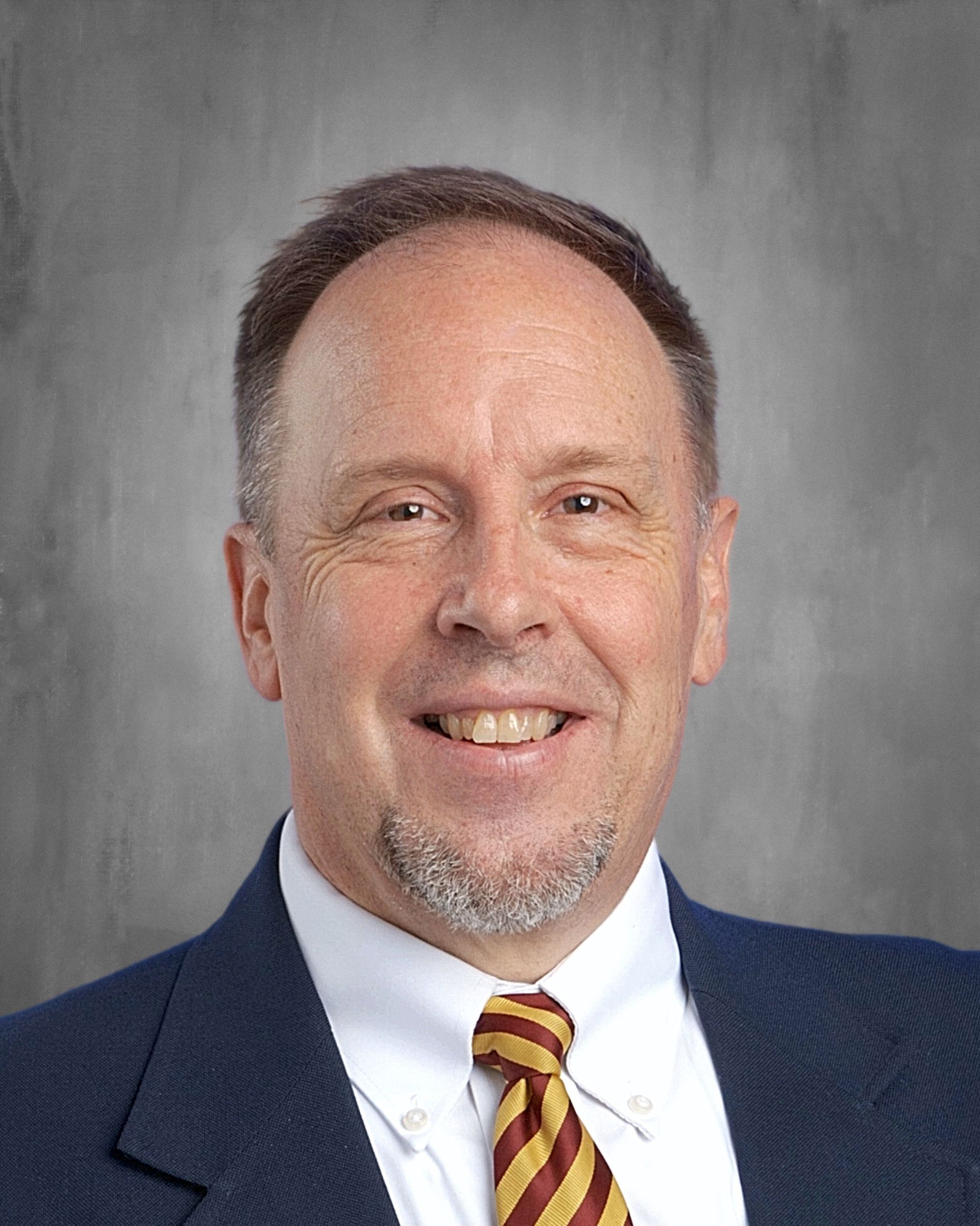 Man in blue suit, smiling, wearing a striped gold and maroon bow tie.