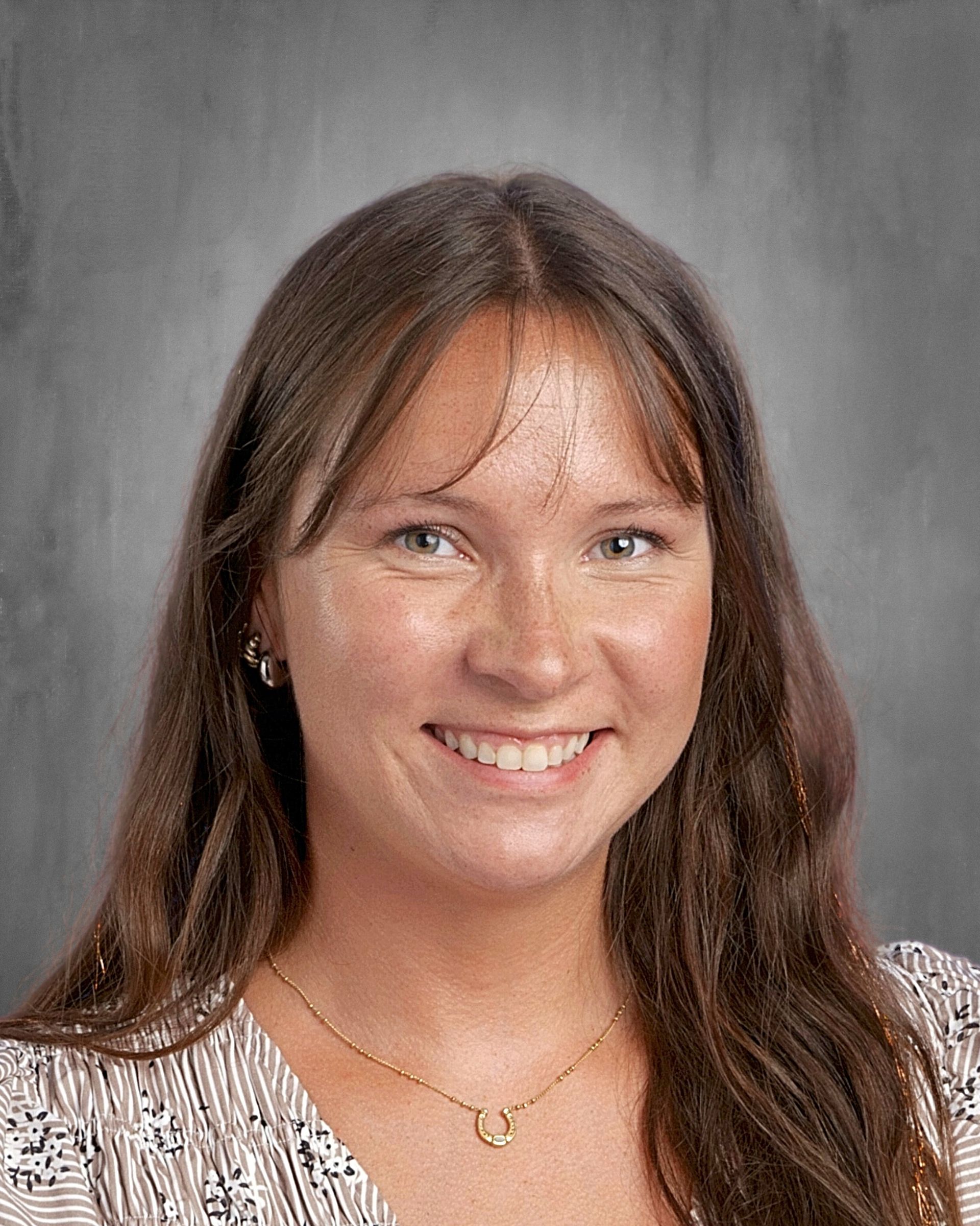 Woman with fair skin smiles, wearing flower-patterned top, white earrings, and brown hair in a ponytail.