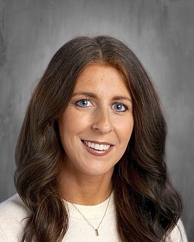 Woman with gray hair and glasses smiling, wearing a blue patterned shirt.