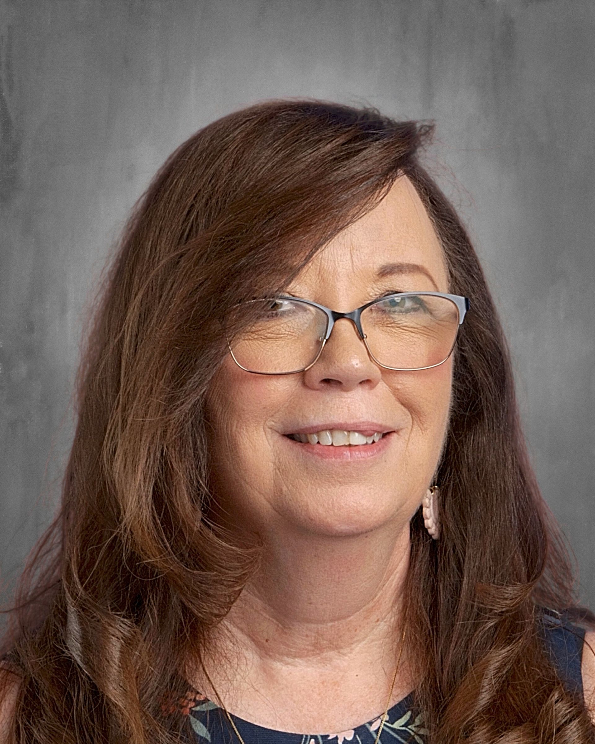 Woman with brown hair, smiling, wearing a patterned top, against a gray background.
