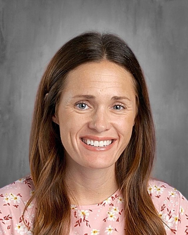Woman with long brown hair smiling at the camera against a gray background.