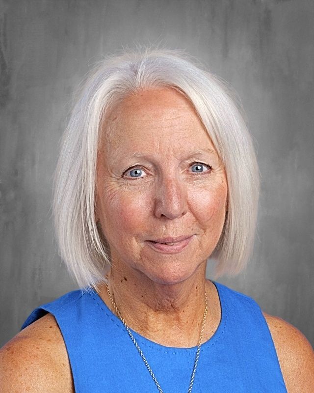 Woman with white hair and blue eyes, wearing a light blue top and pearl necklace, smiling.