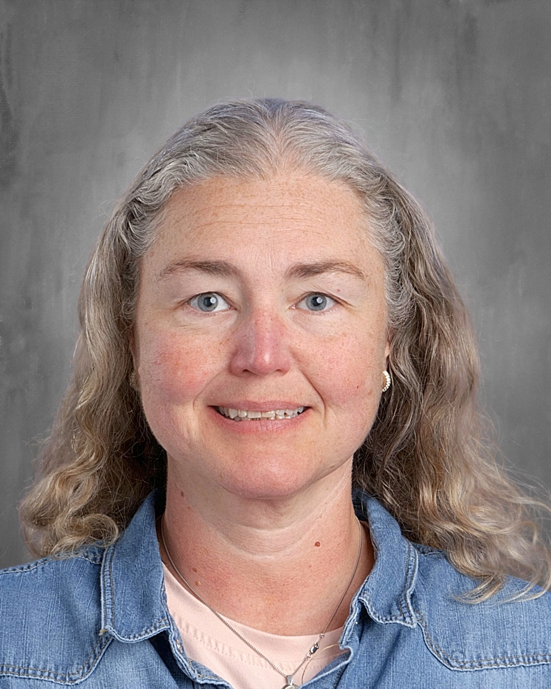 Woman with graying curly hair smiles; neutral background.