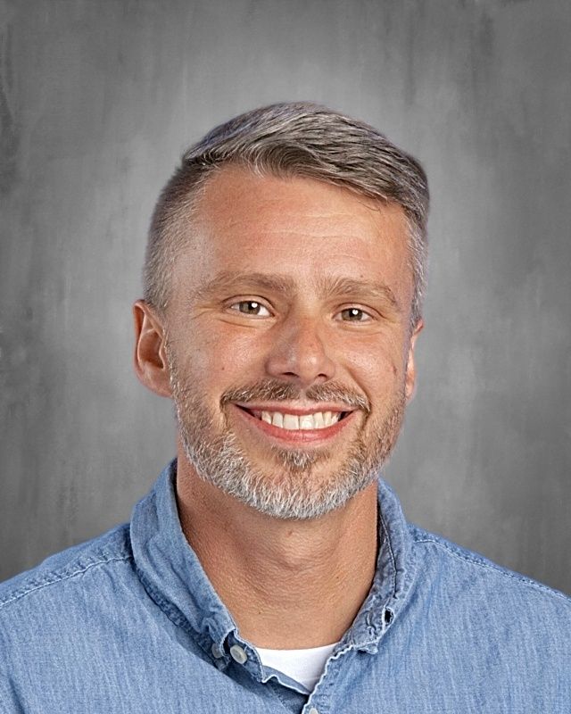 Woman with glasses smiling, wearing an orange top, against a gray backdrop.
