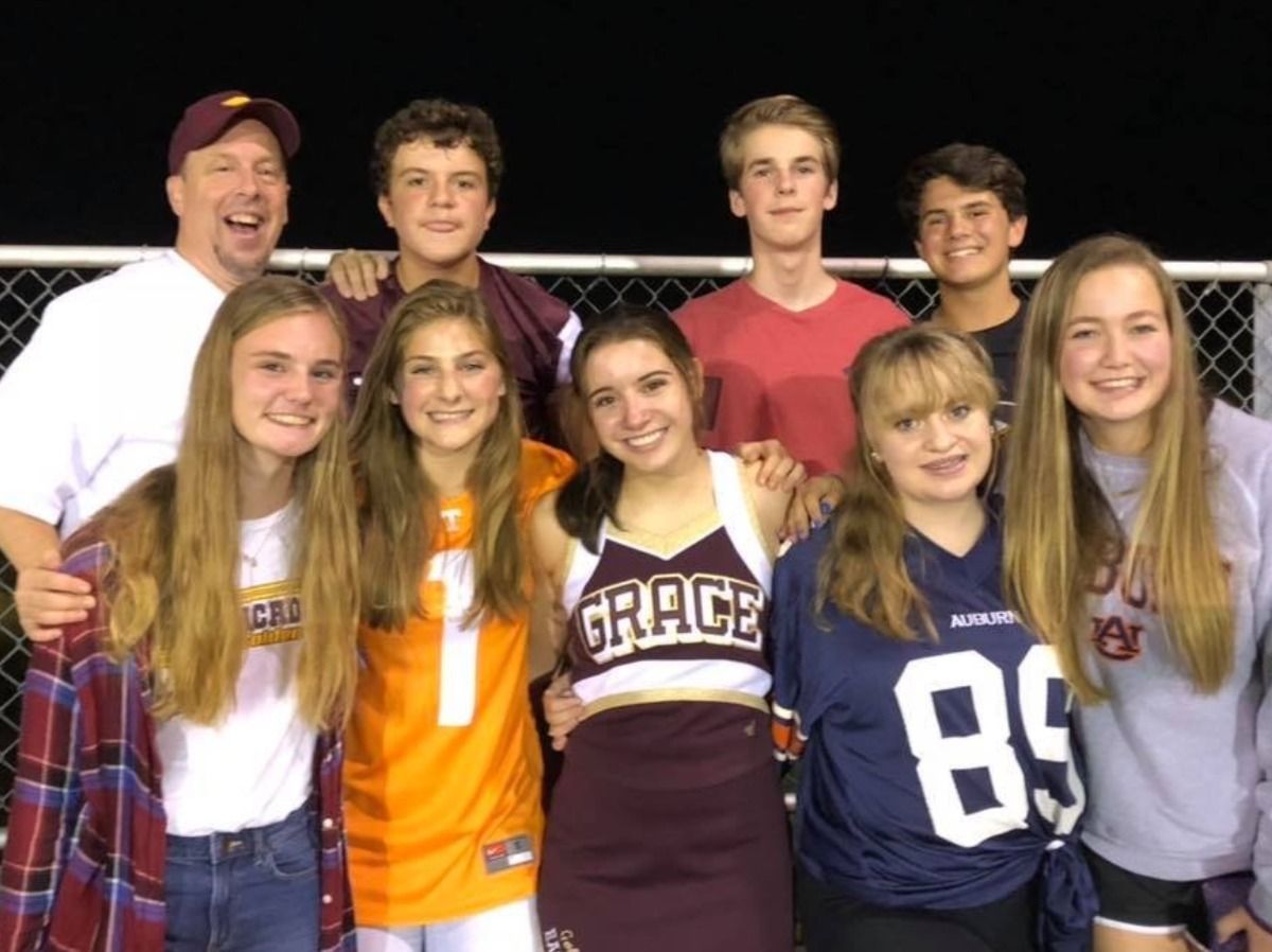 Group of people smiling at a football game. People in team colors, a cheerleader in the middle.