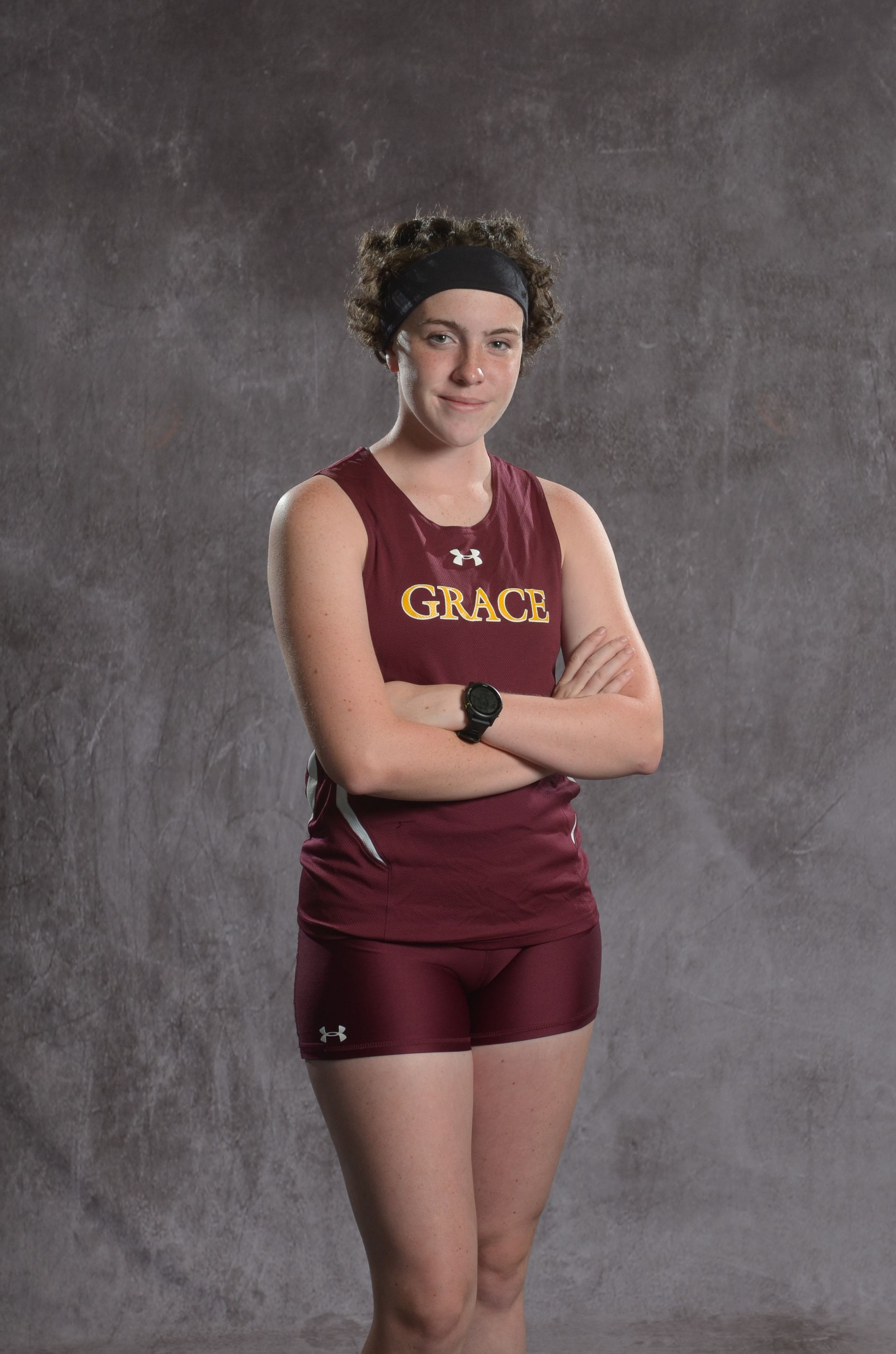 Bald female athlete on a track, arms crossed, wearing maroon uniform.