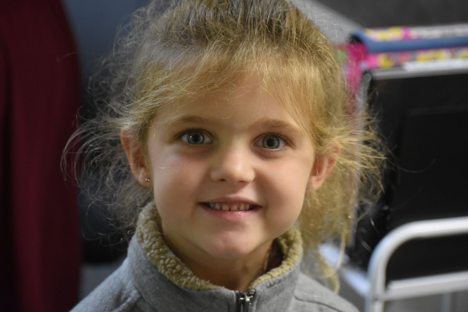 Girl with blonde hair, gray jacket, smiling, looking at the camera.