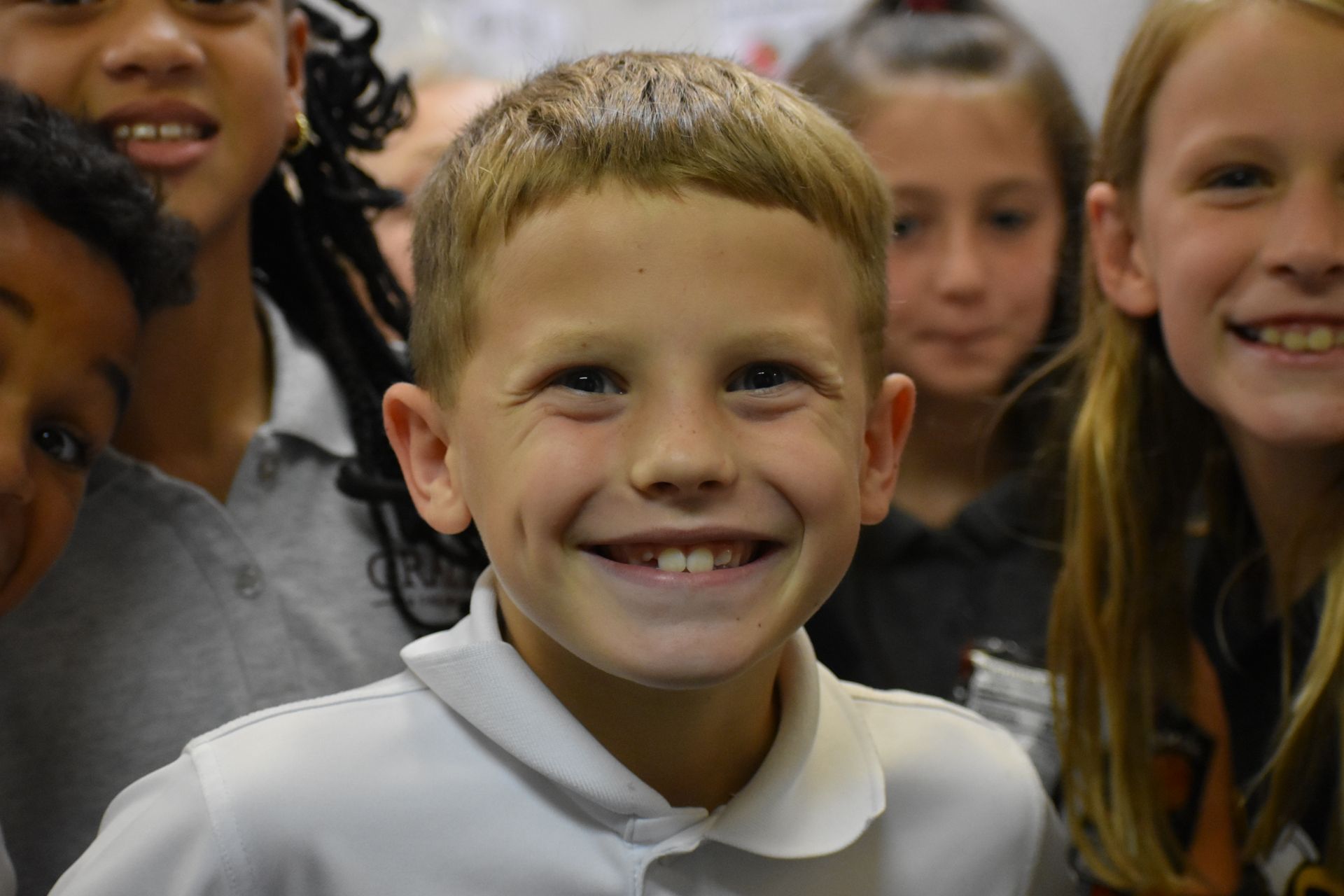 Boy with dimples smiles, surrounded by classmates in a school setting.