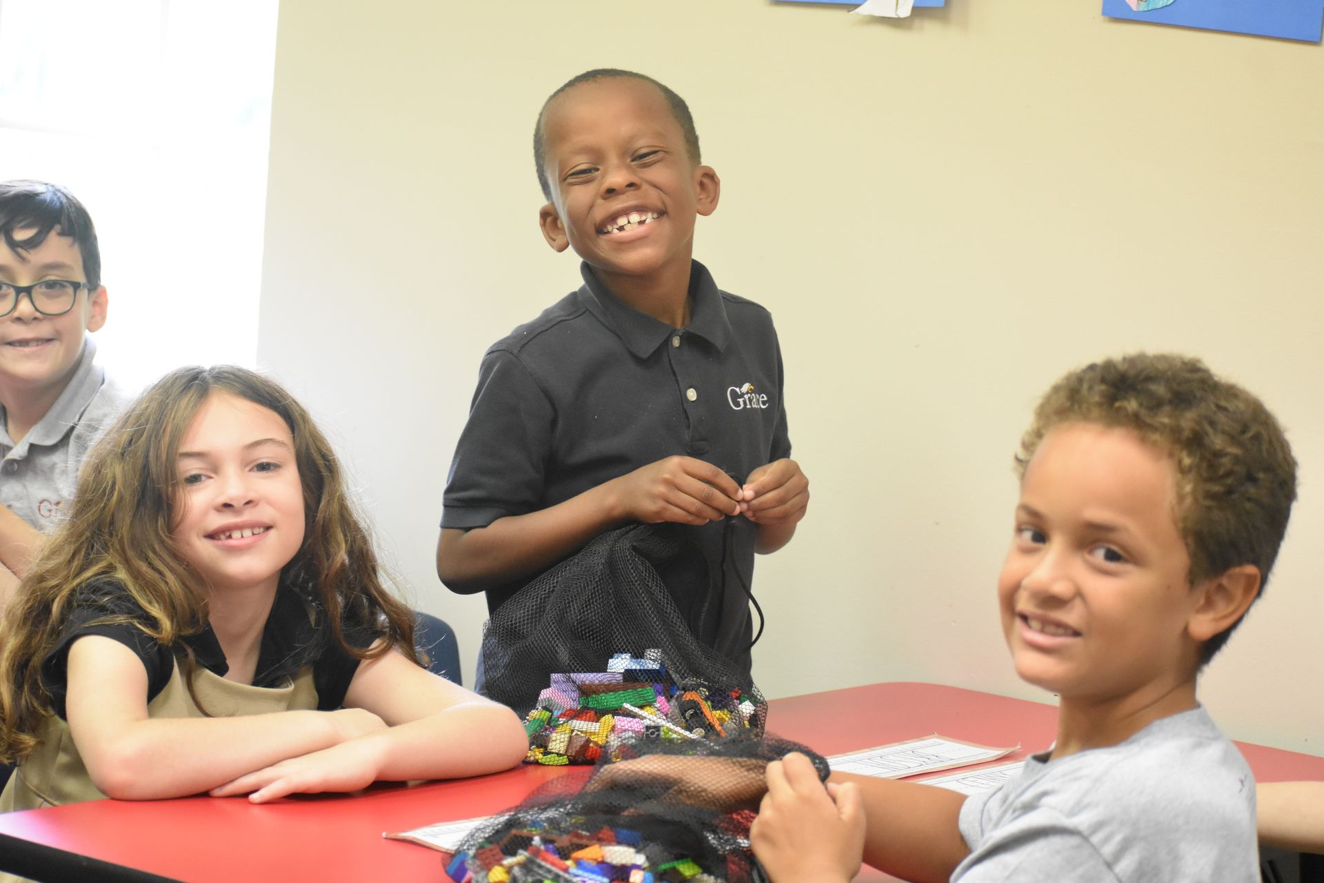 Four children smiling at a red table in a classroom.