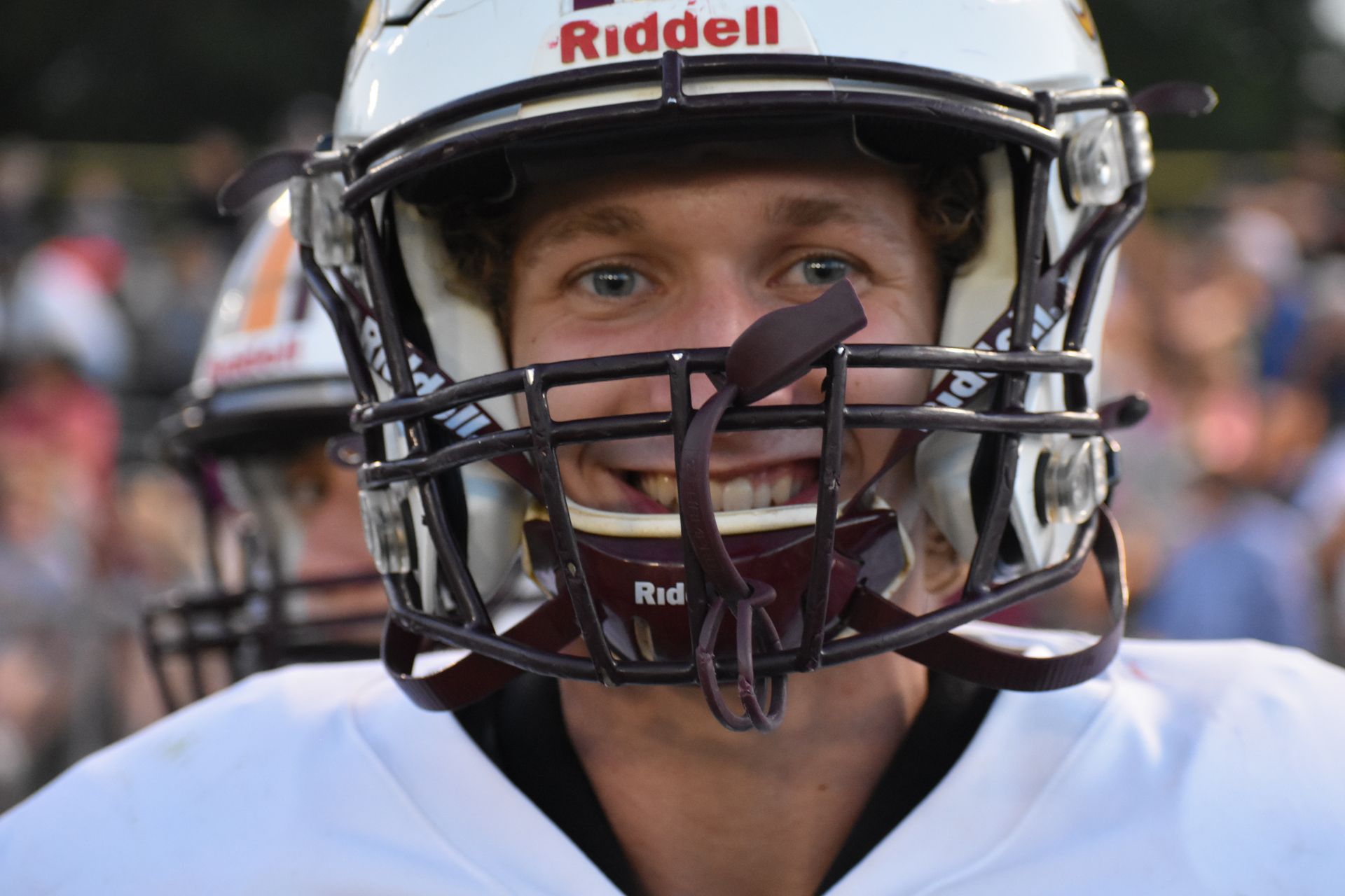 Football player in a helmet smiling, close-up. Wearing brown and white uniform, outdoors.