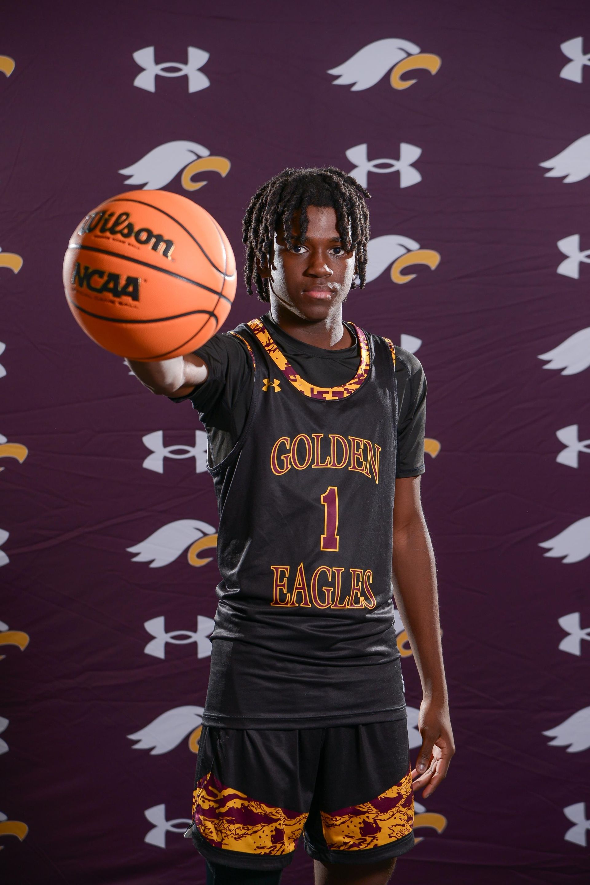 Basketball player in black and gold jersey spins ball on finger, pointing at viewer.