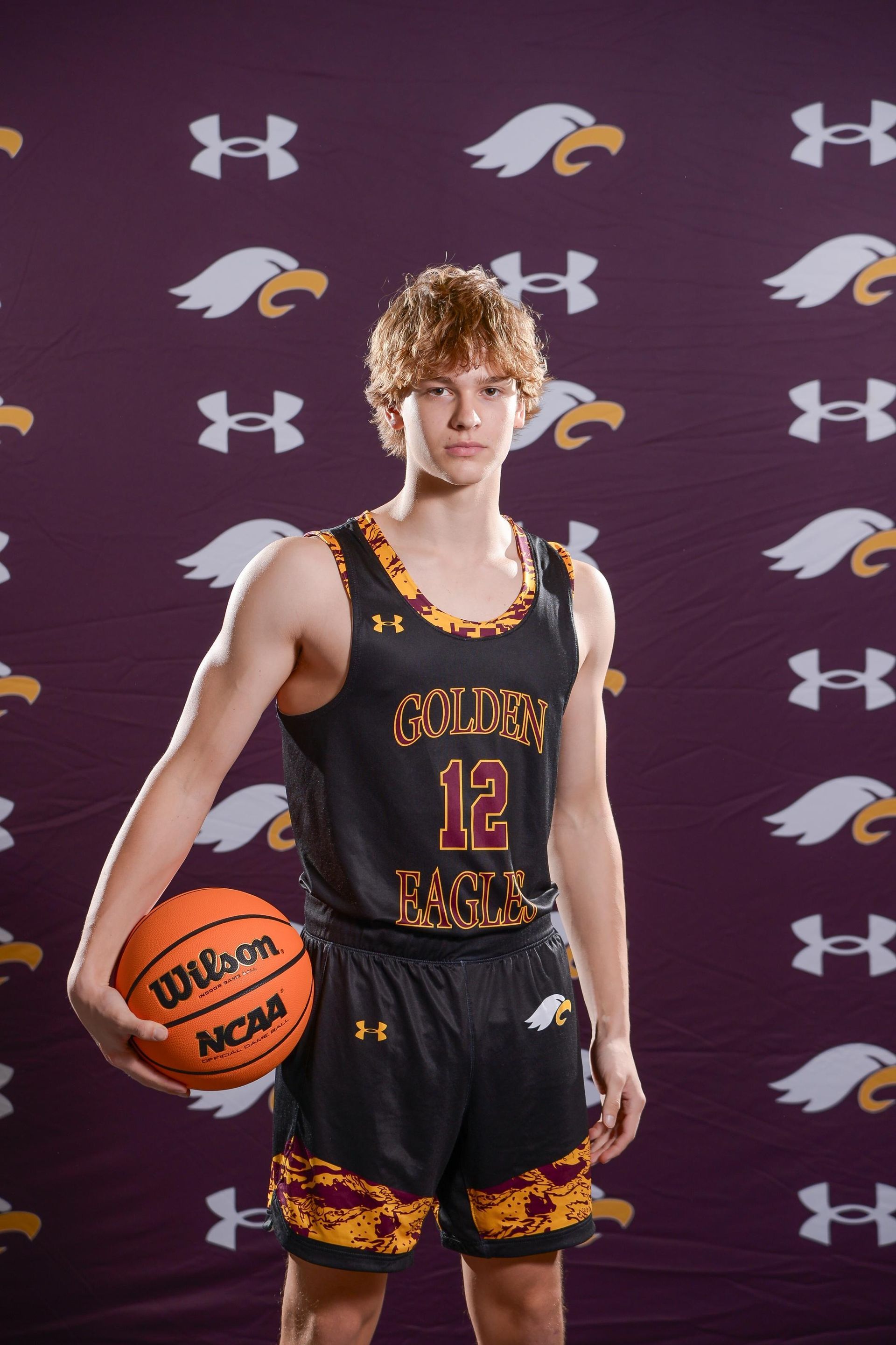 Teen basketball player in black and gold jersey holding a basketball. Dark background.