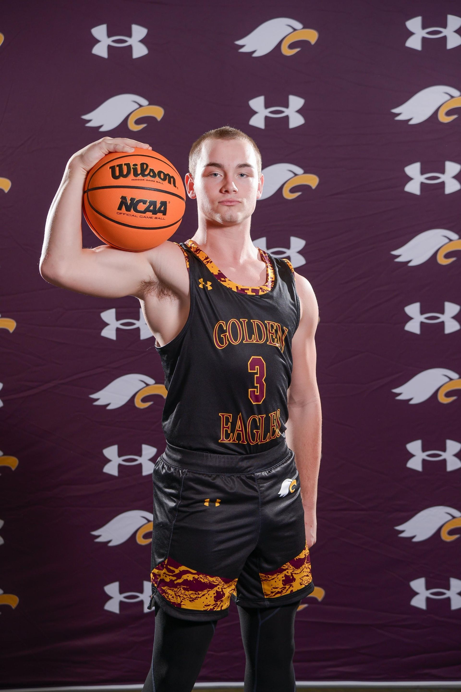 Basketball player in black and gold jersey spinning a ball on one finger, pointing at the viewer.