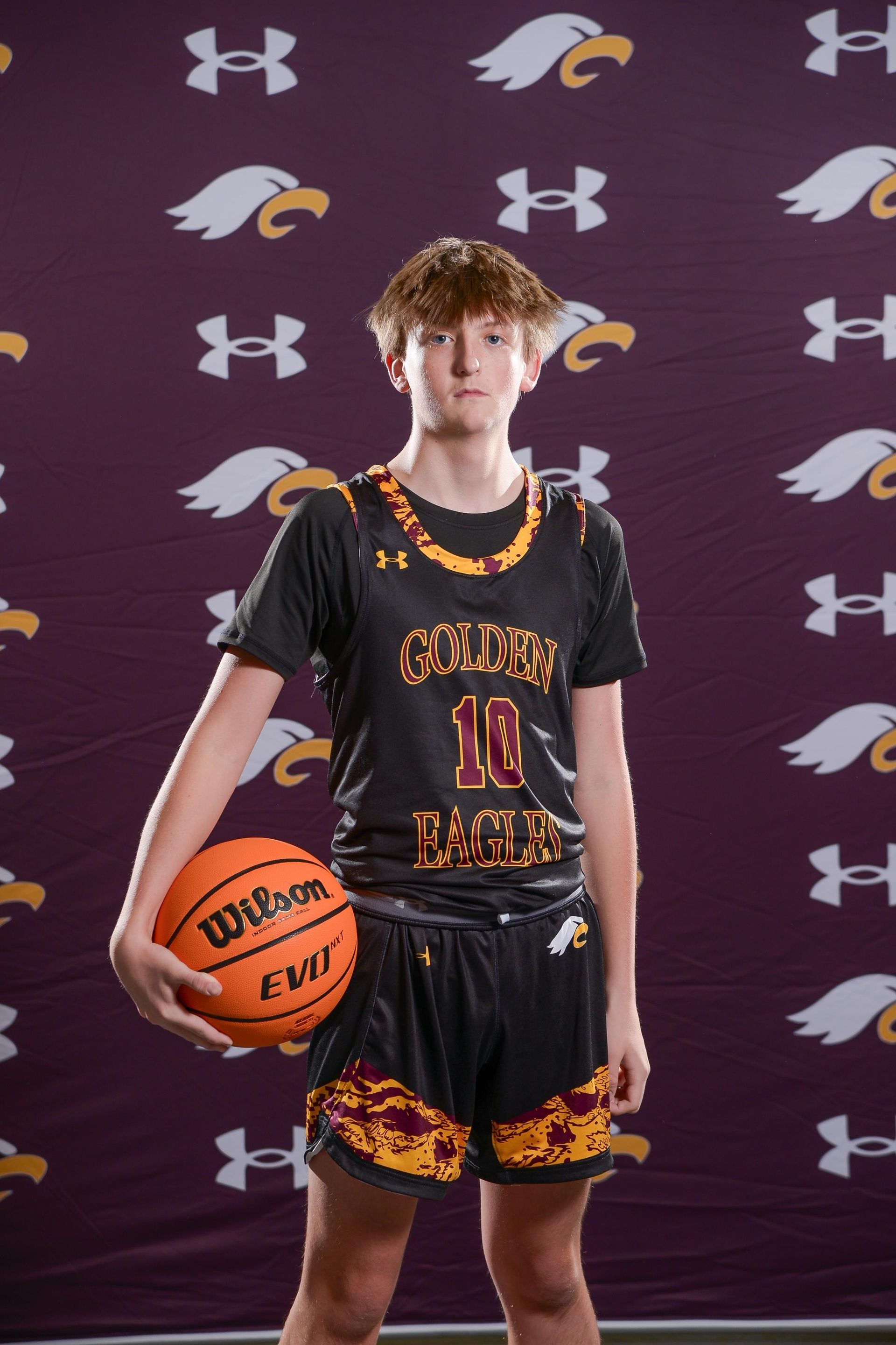 Basketball player in a black and gold jersey spins a ball, points, dark background.