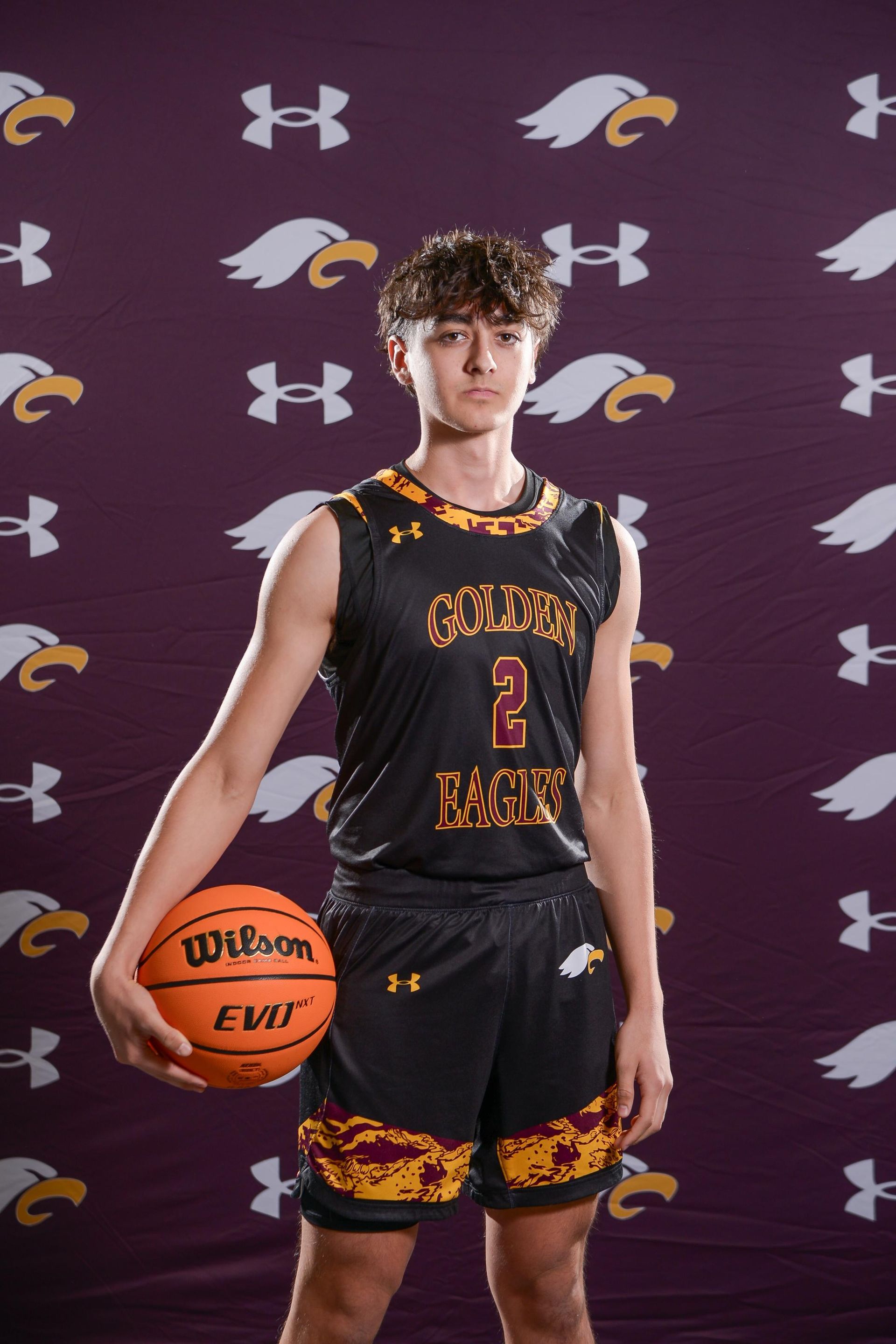 Basketball player in black and gold jersey holding an orange Wilson basketball, smiling against a black backdrop.
