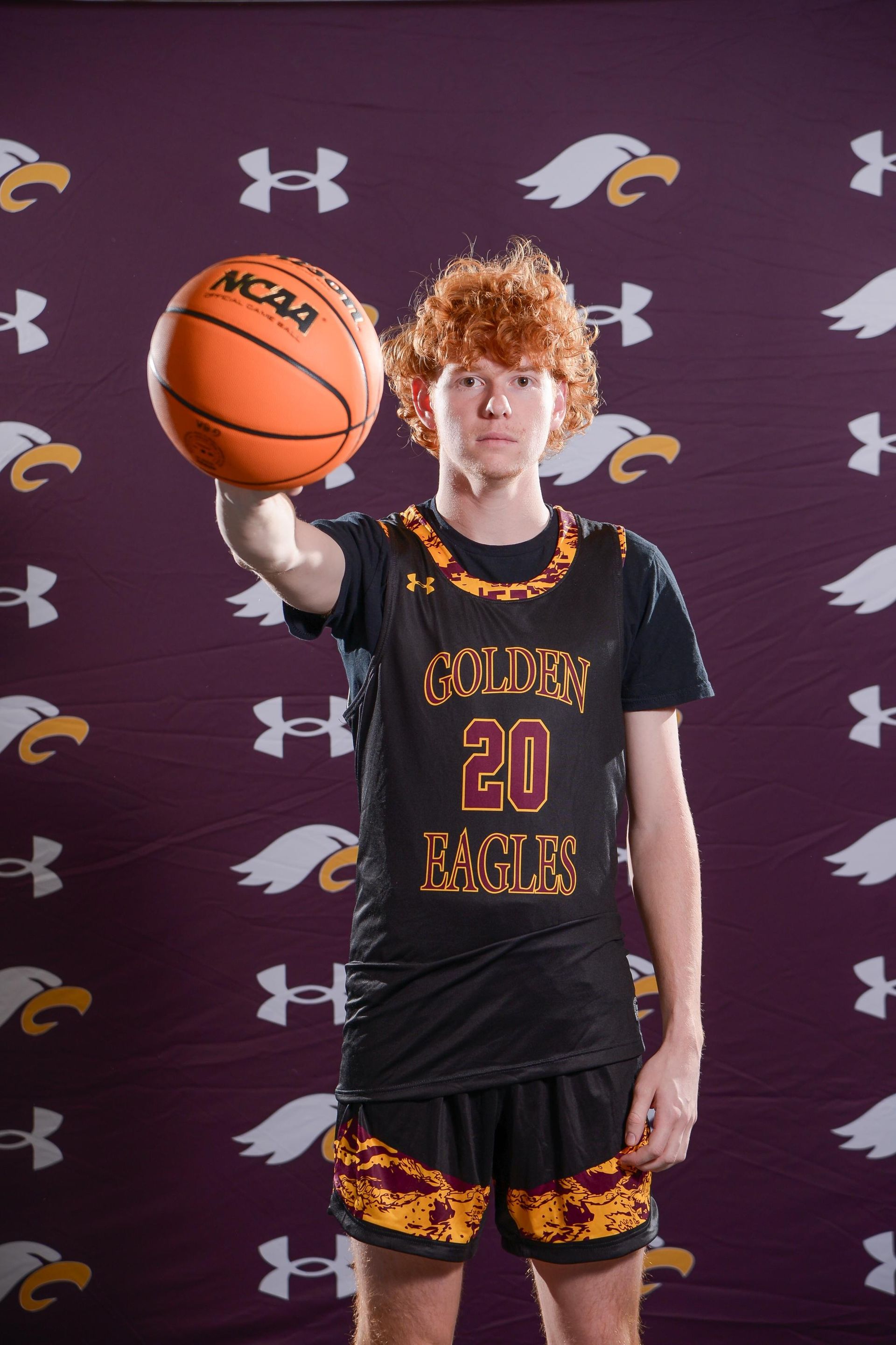 Teenage basketball player in Golden Jaguars jersey holds ball, black background.