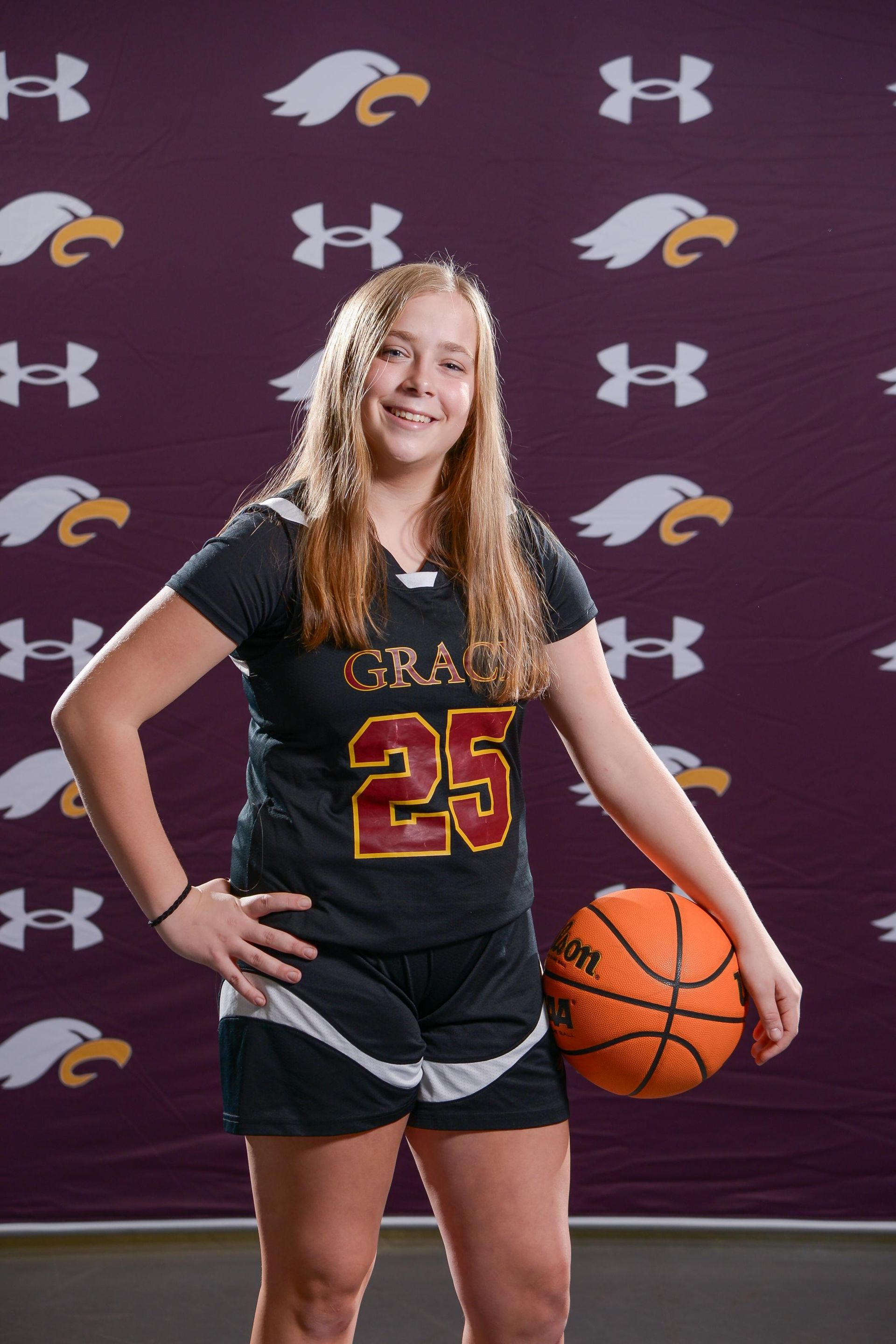 A teenage girl in a maroon basketball jersey holding a basketball.
