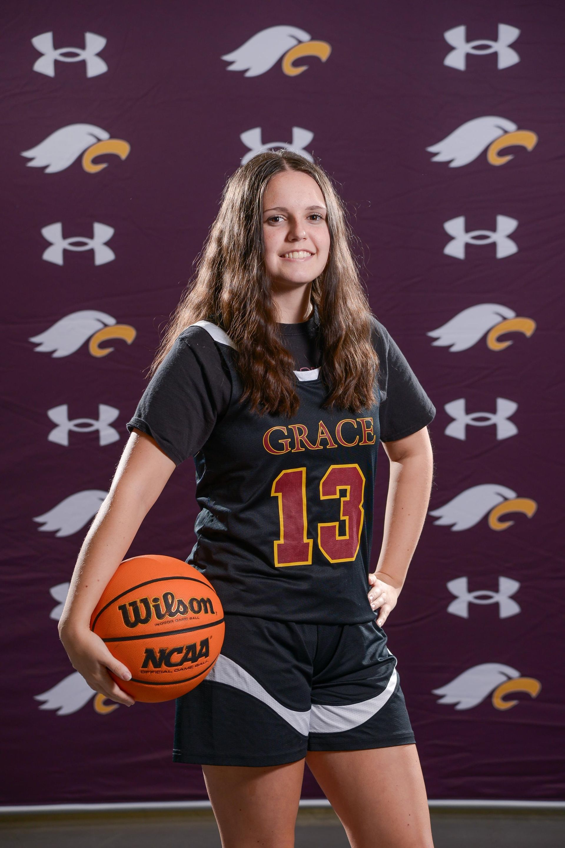 Female basketball player in maroon jersey, holding ball, posing for photo.