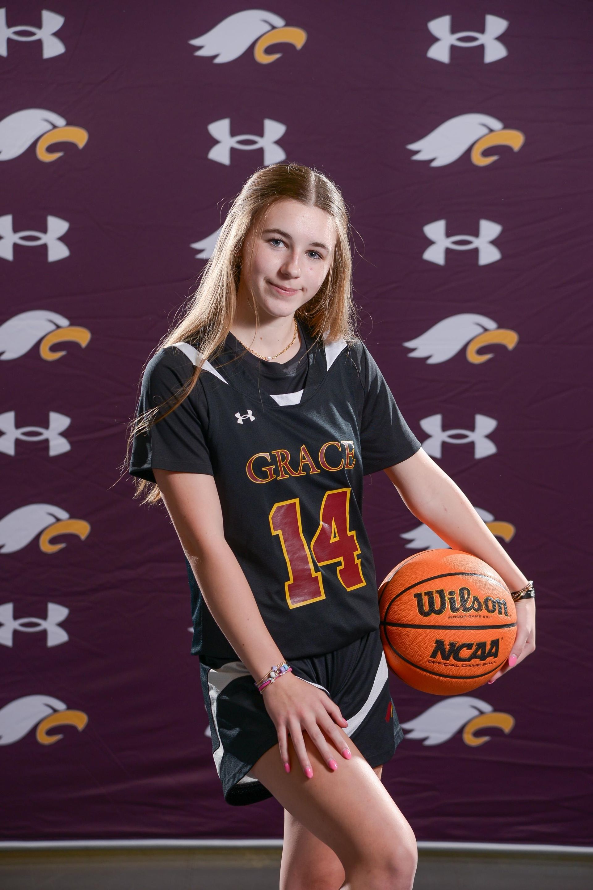 Young basketball player in maroon uniform with ball, smiling.
