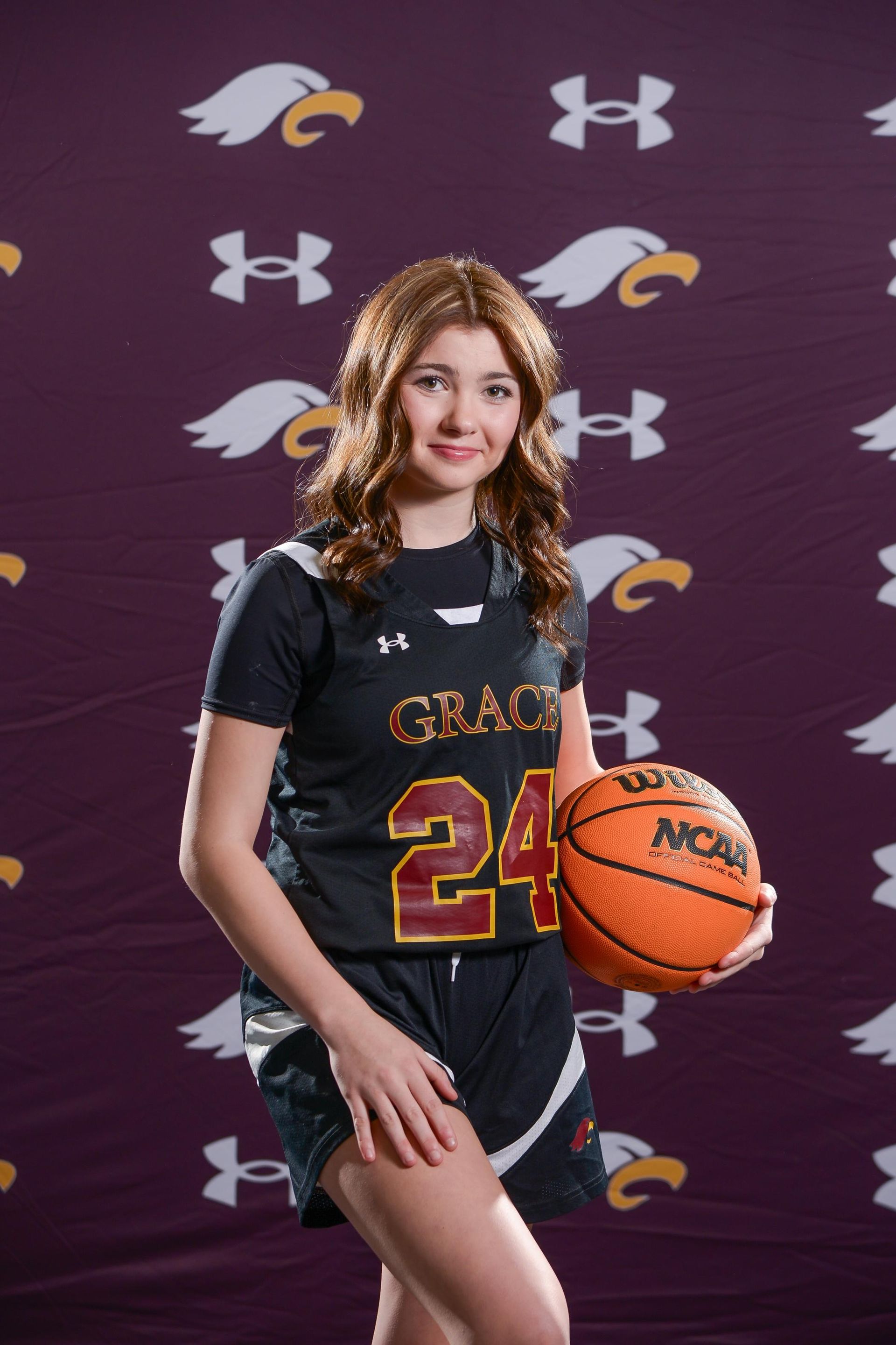Young woman in maroon basketball jersey (#24) holding a basketball, smiling.