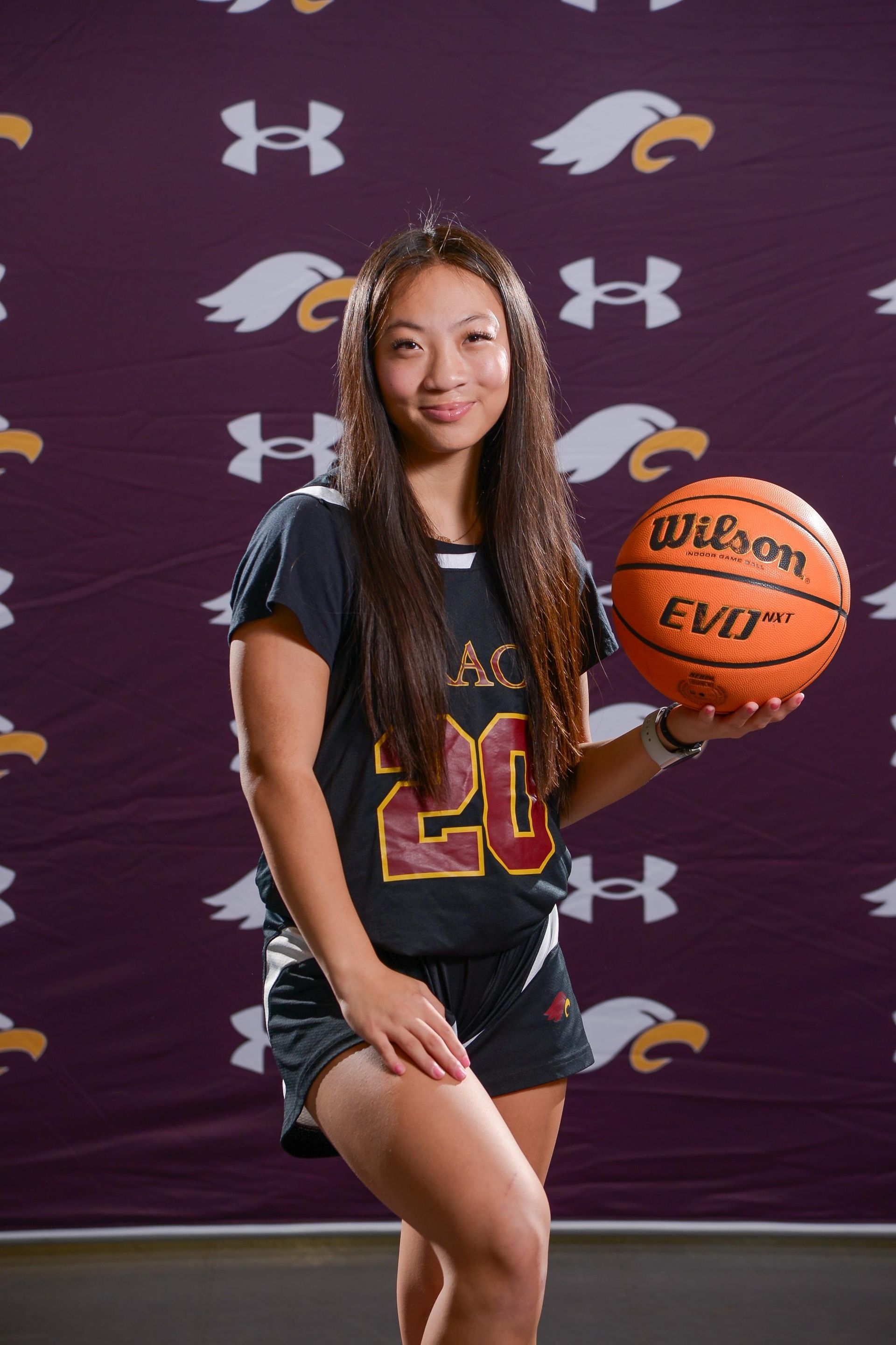 Young woman in basketball jersey holds a basketball.