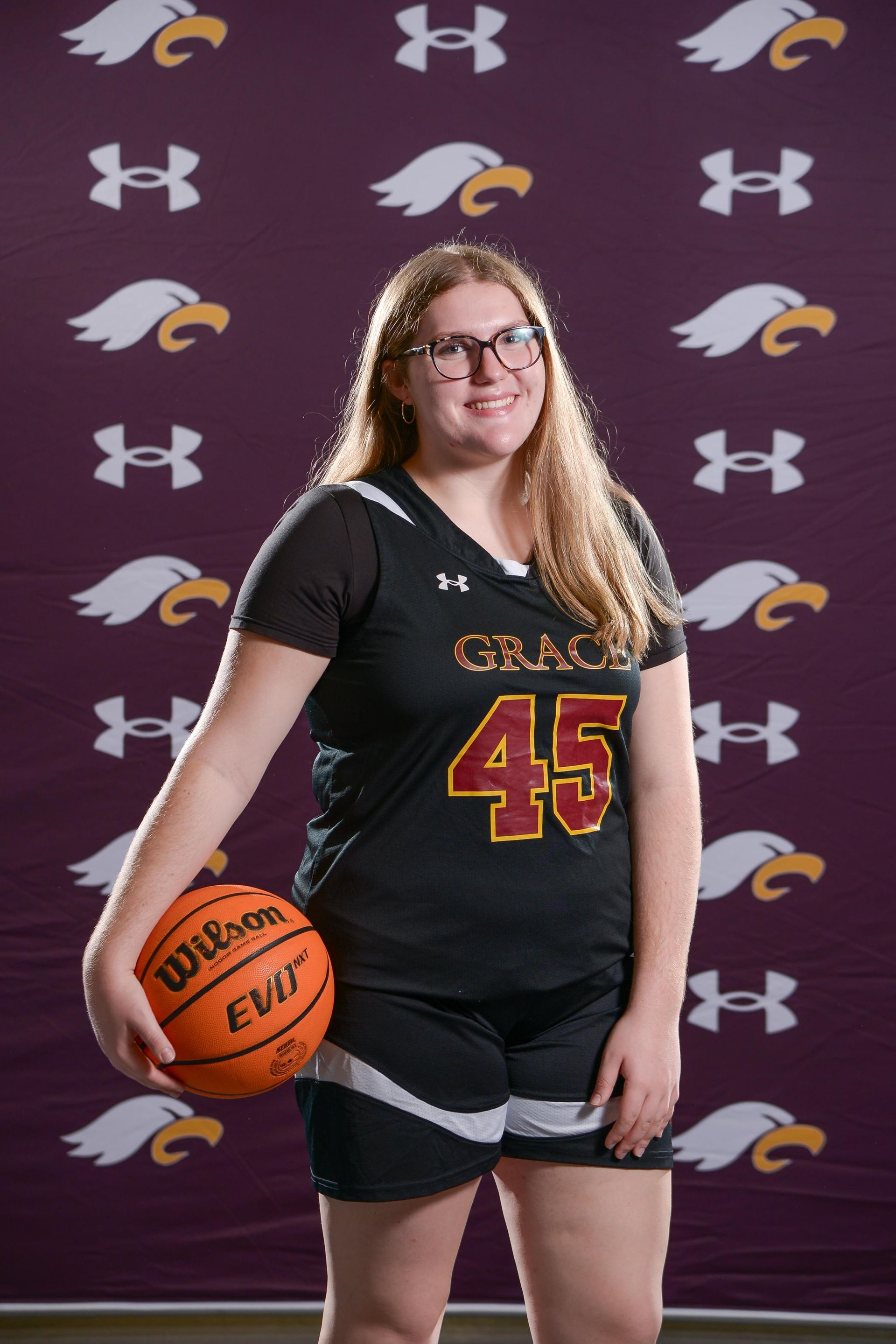 Female basketball player in maroon jersey with ball, smiling.