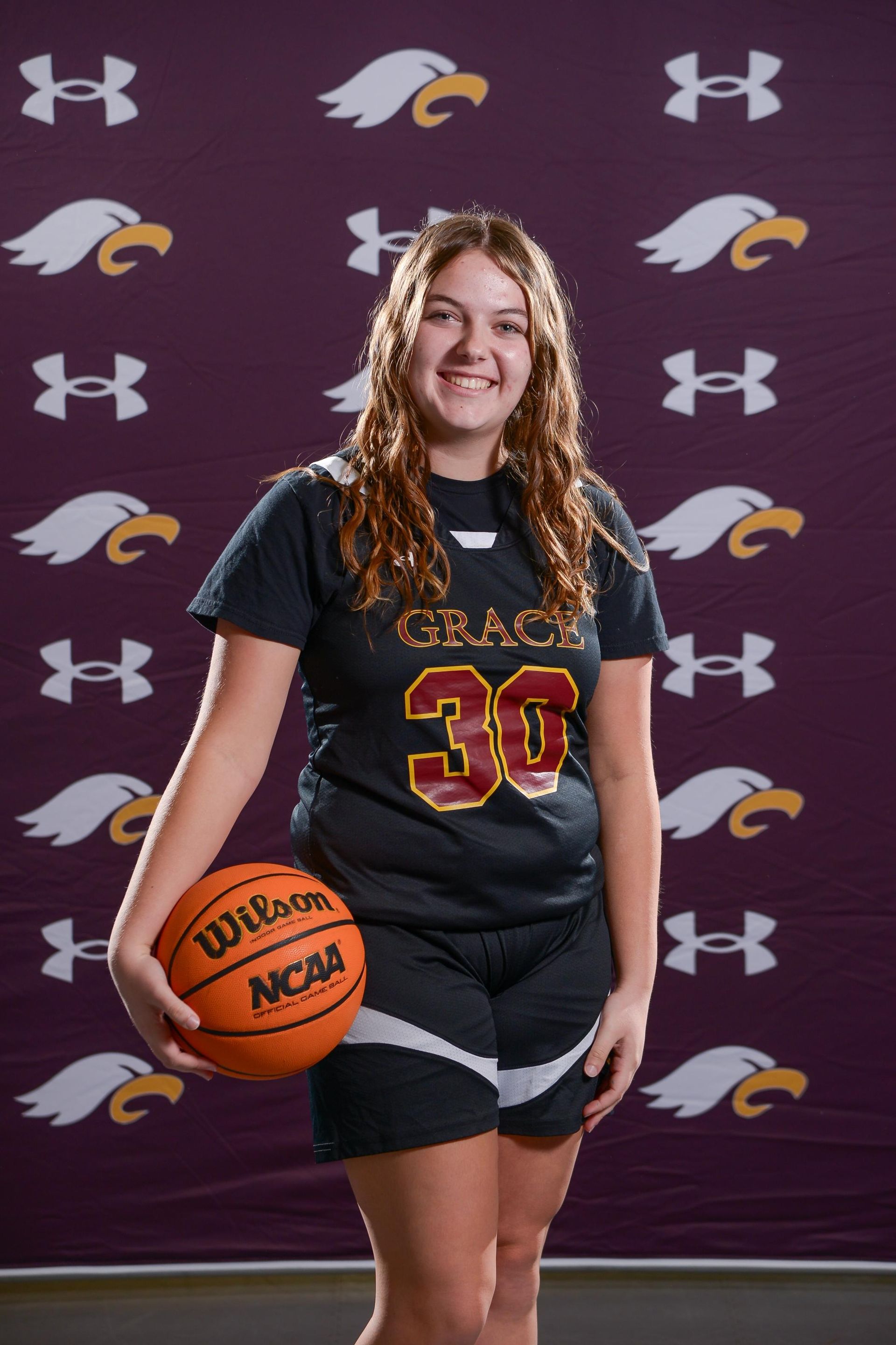 Basketball player in maroon jersey holding a ball, smiling. 