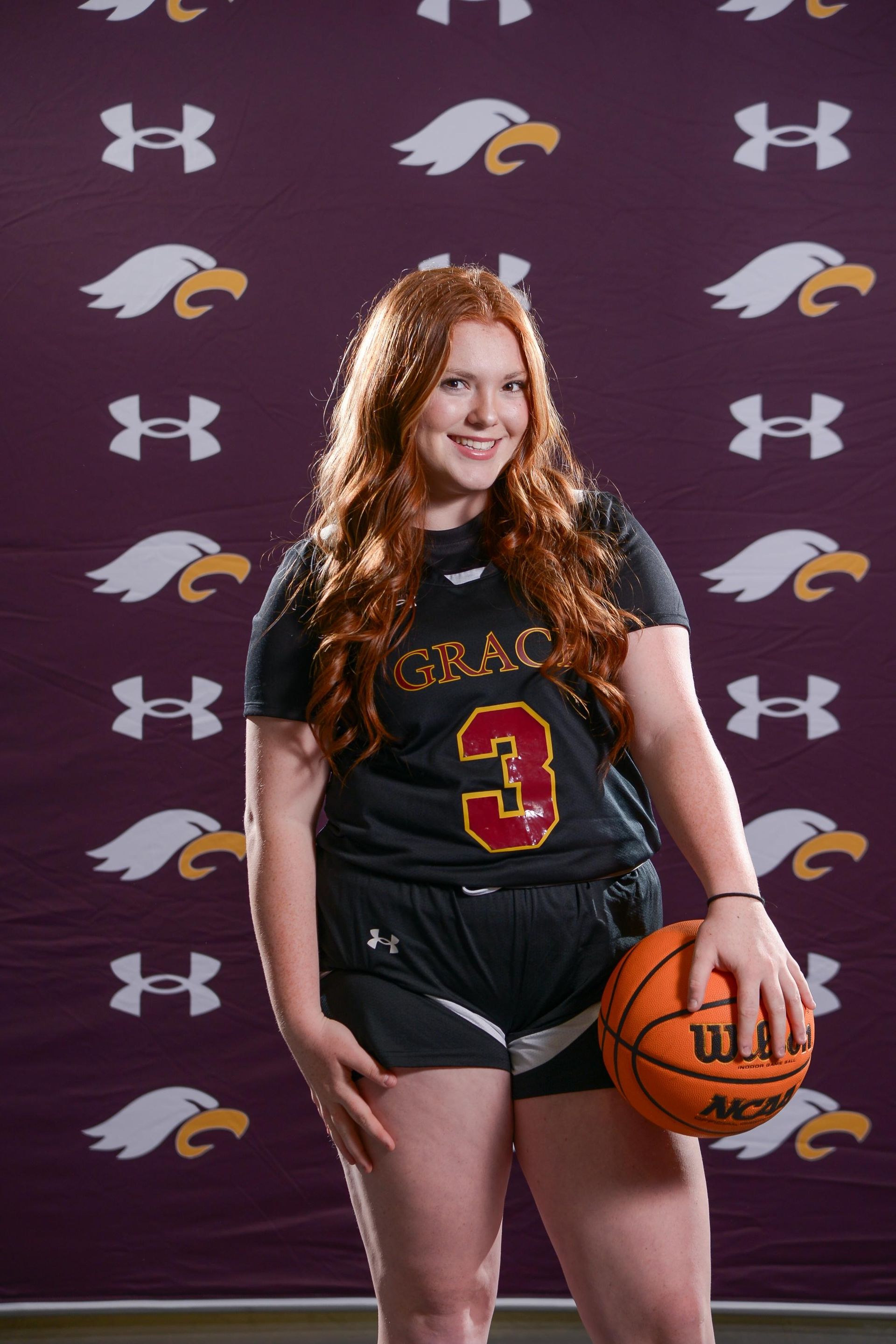 Woman in maroon basketball uniform holding a basketball, smiling.