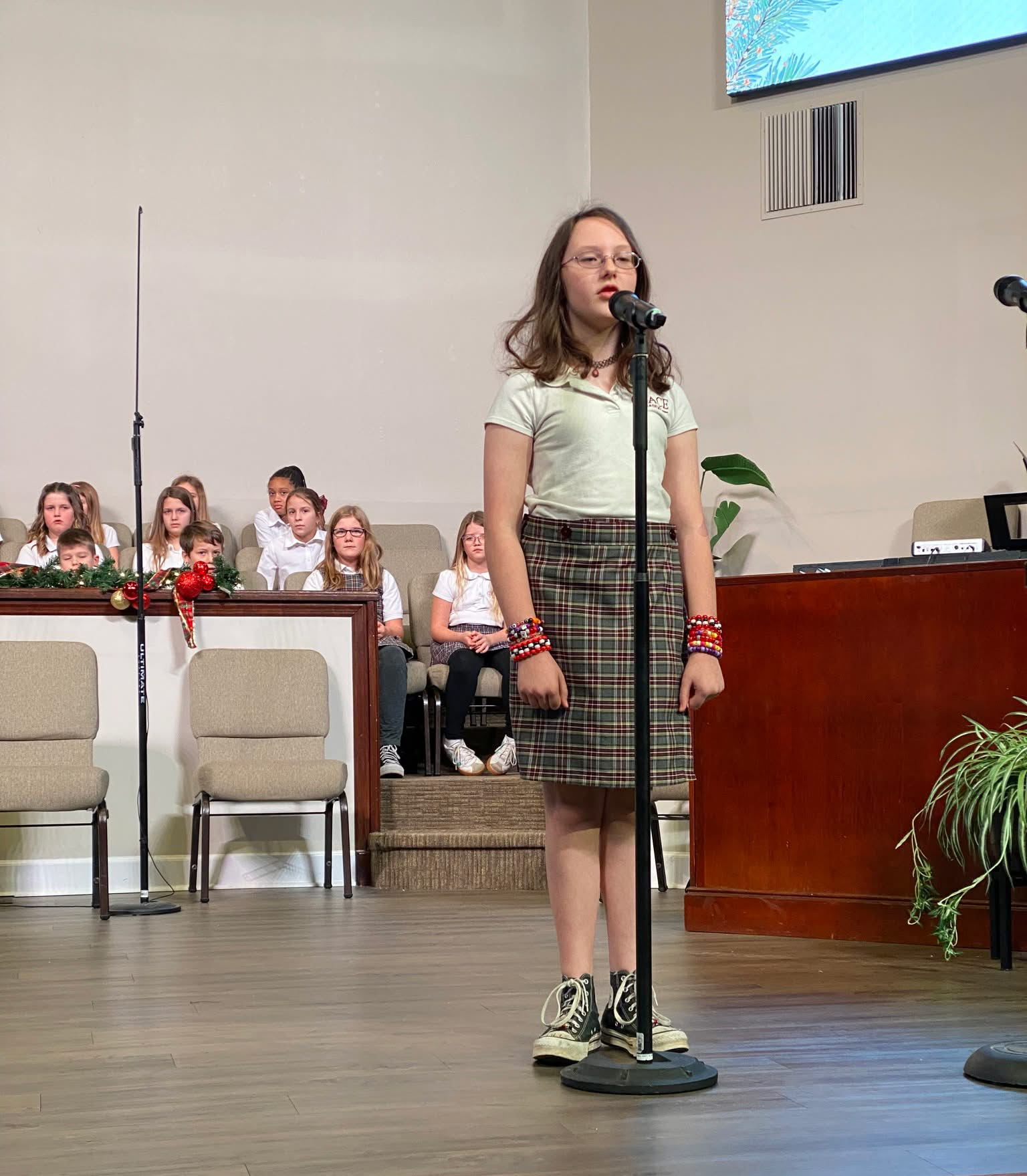Four smiling children in school uniforms, two boys and two girls, posing indoors.