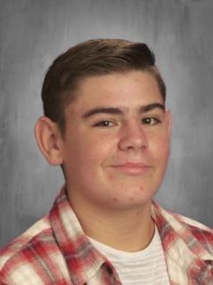 Teenager with light skin wearing a plaid shirt, smiling.