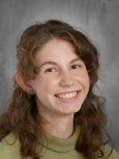 Woman with long brown hair smiles, wearing a light green turtleneck.